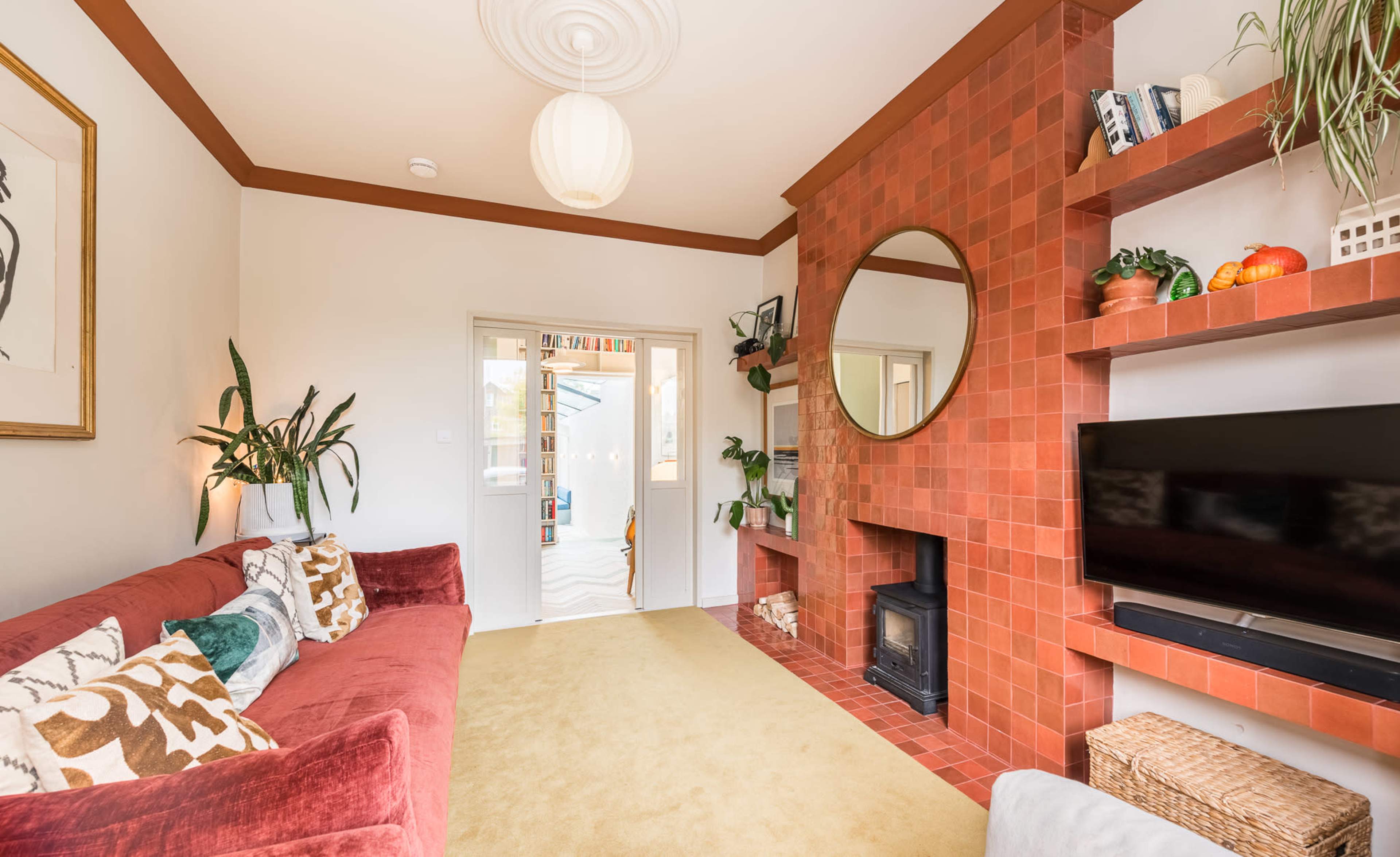 The living room features a red tiled fireplace, a large circular mirror, and a cozy red sofa with decorative pillows.