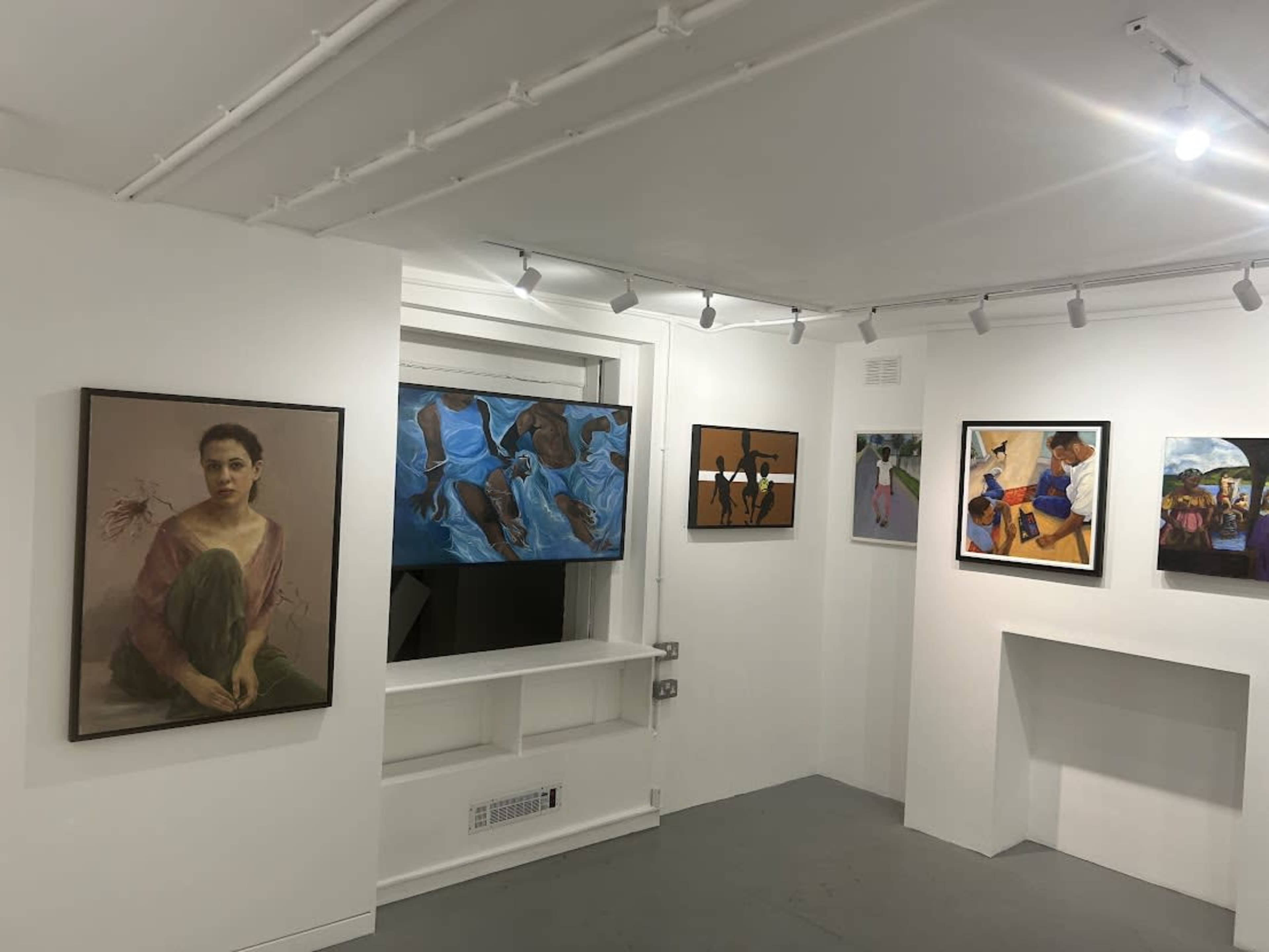 An art gallery with several paintings displayed on white walls, featuring a variety of subjects and styles.