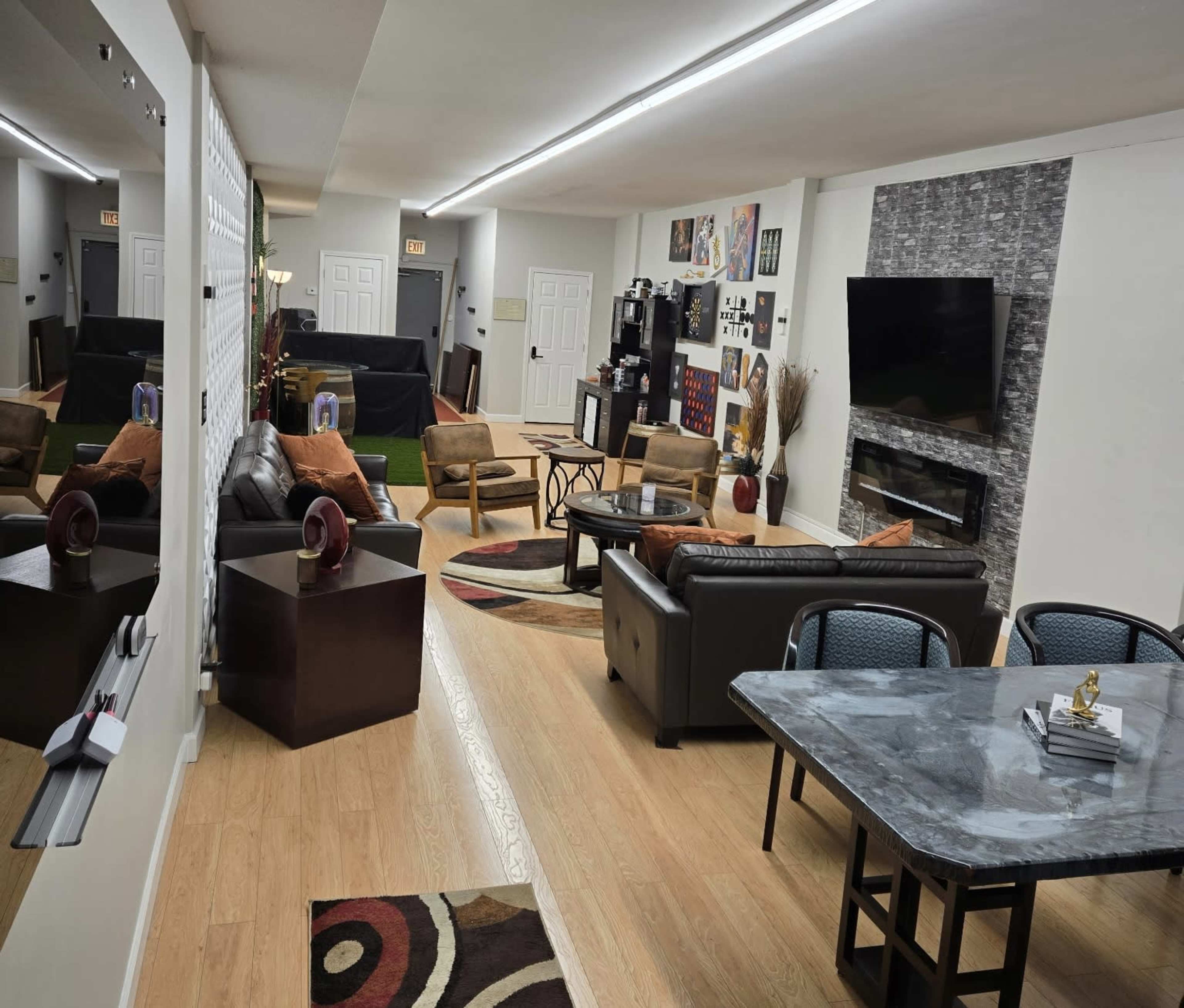 The image shows a spacious, modern lounge area with contrasting dark and light furniture, decorated with various artworks and a large wall-mounted TV.