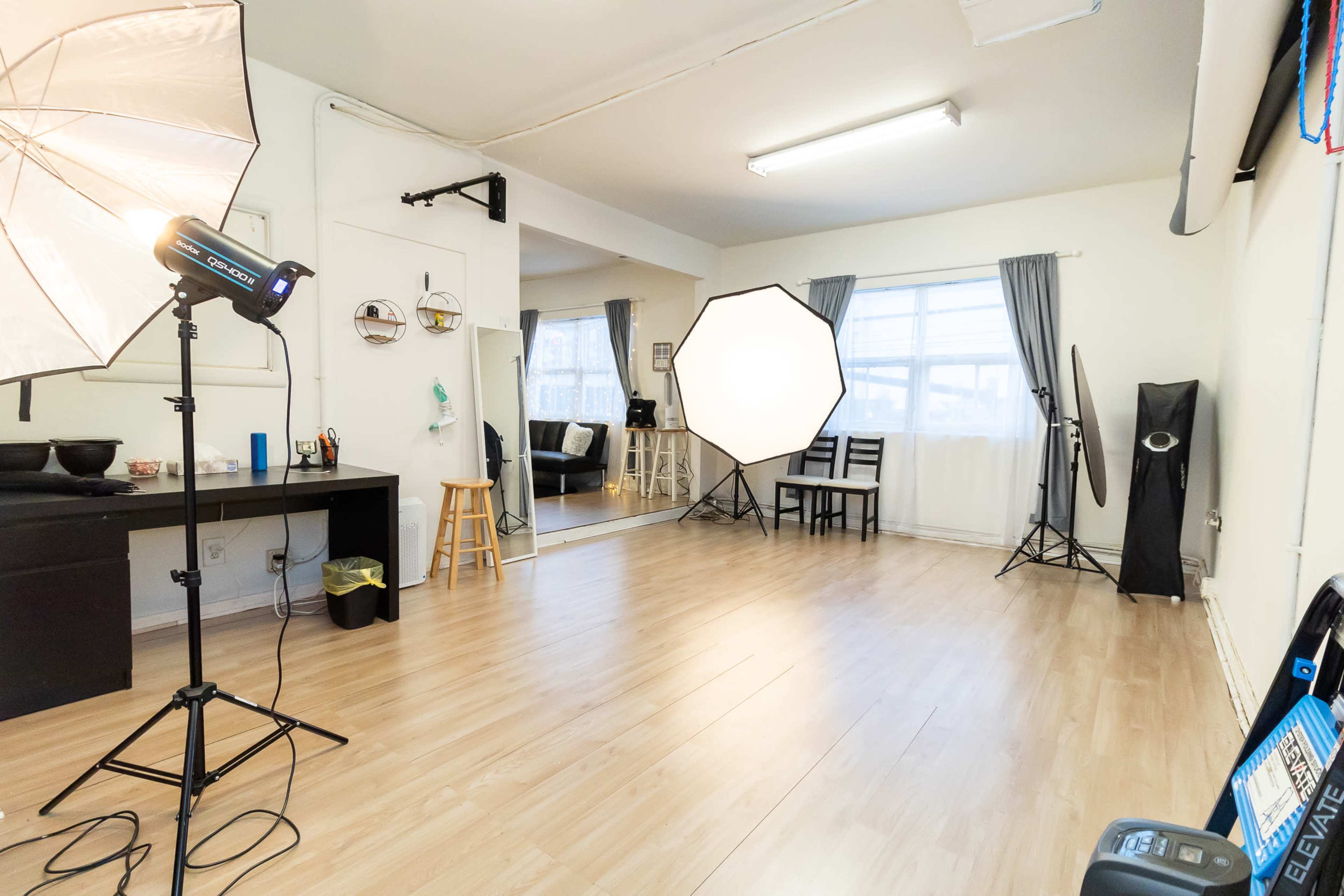 The image shows a photography studio with lighting equipment, a mirror, chairs, and wooden flooring.