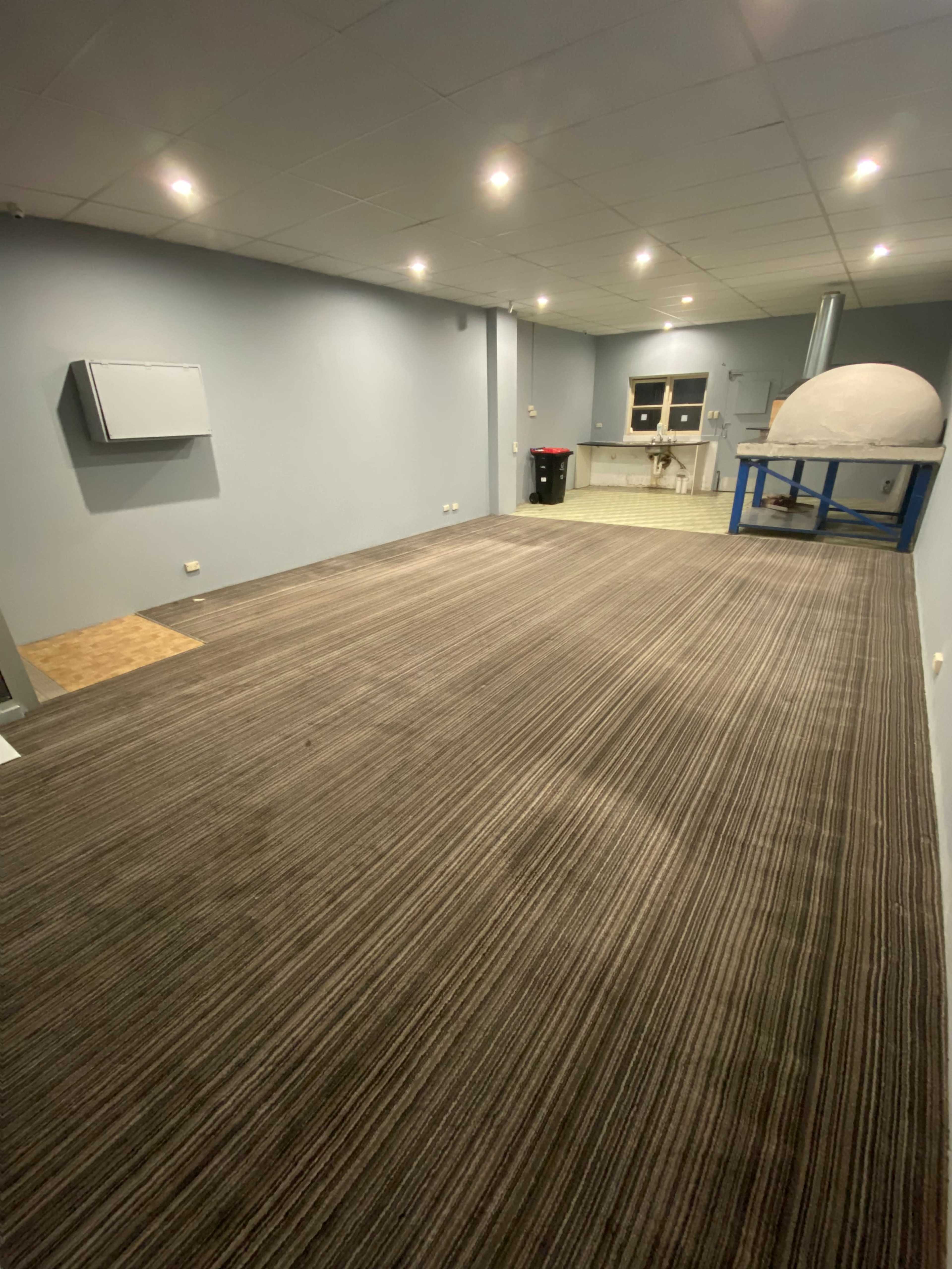 A spacious room with a carpeted floor, overhead lights, and a wall-mounted air conditioning unit.