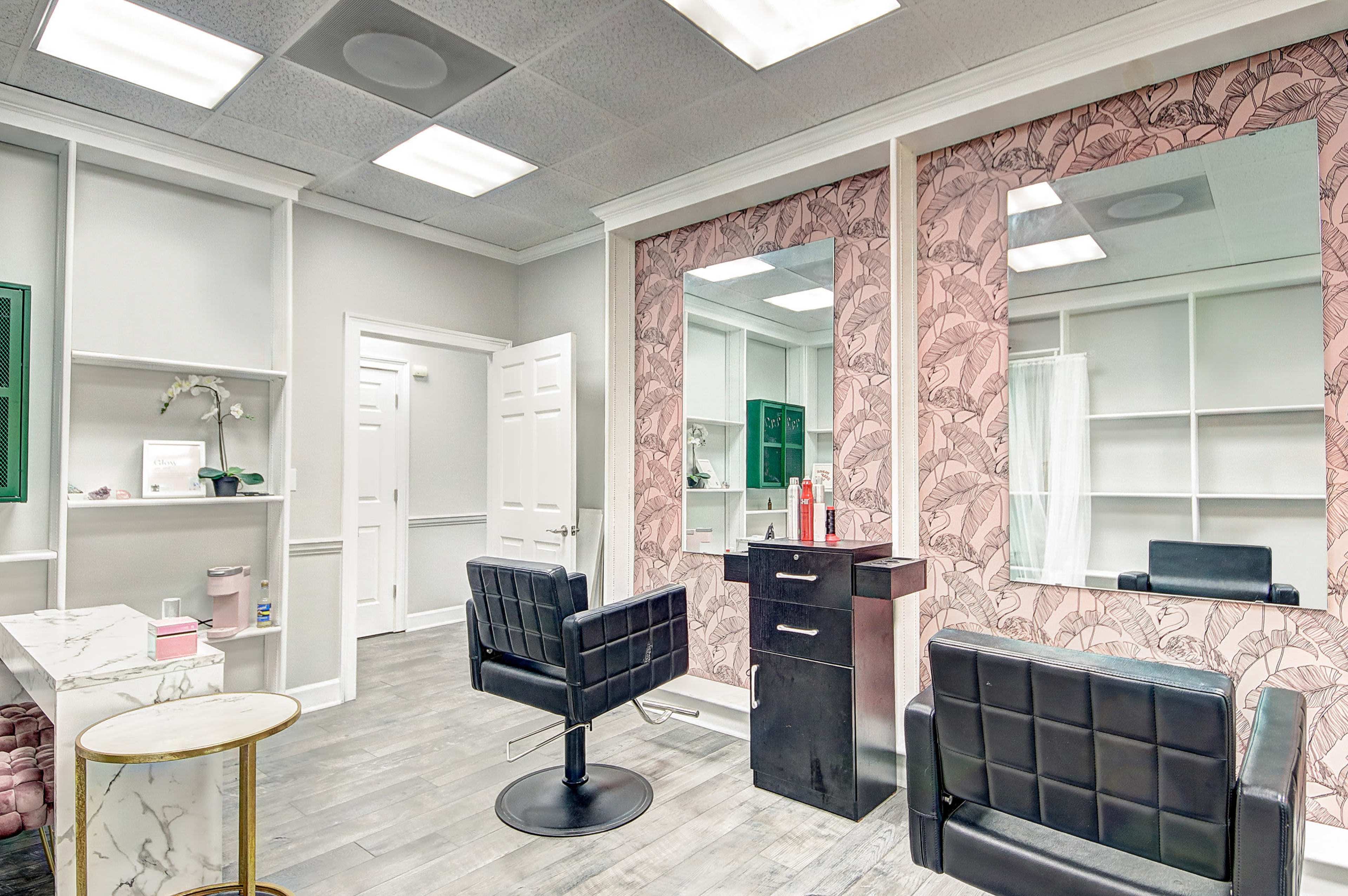 A hair salon interior with two large mirrors, black leather styling chairs, and a light-colored decorative wall with a floral pattern.