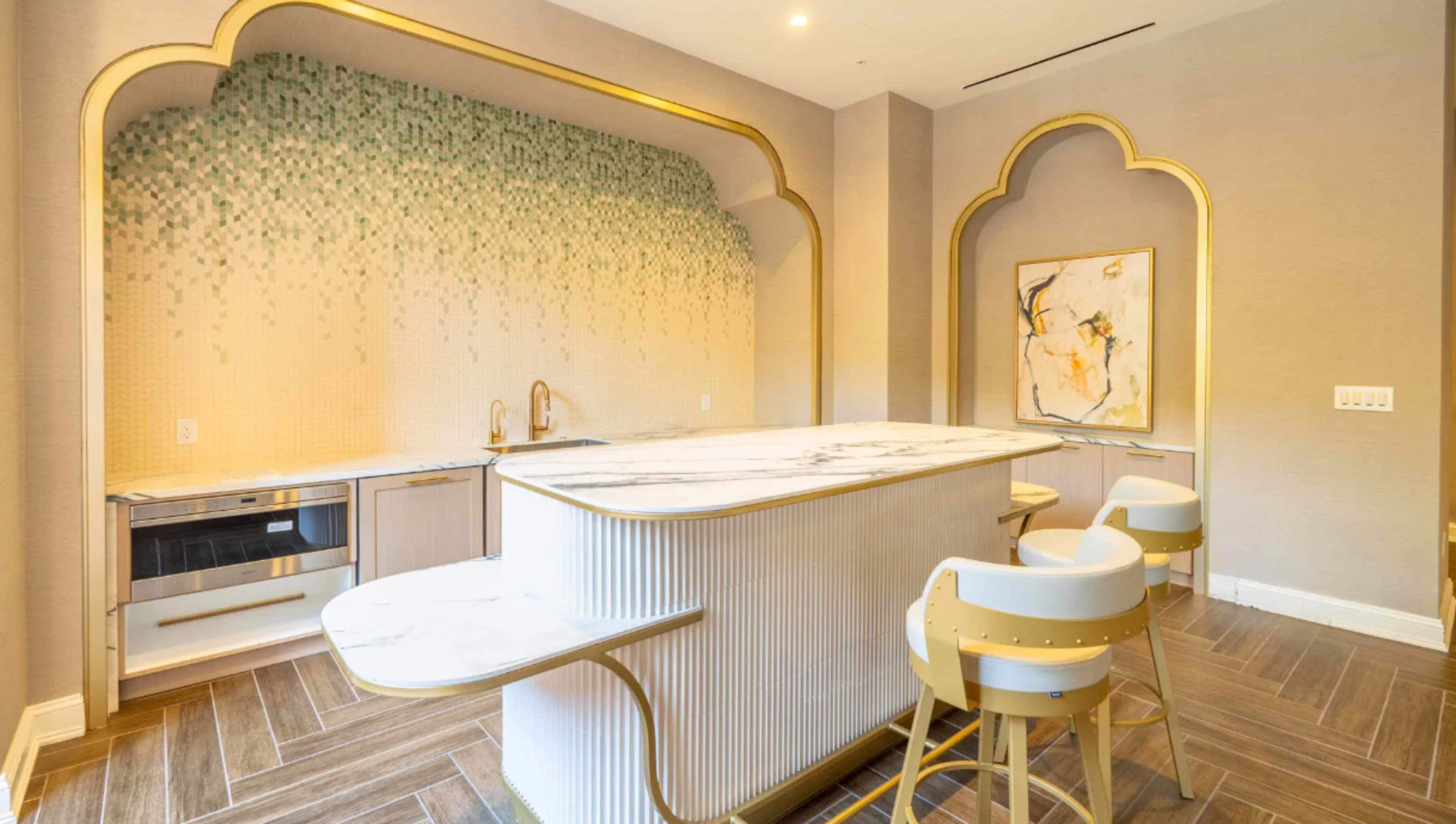 The image shows a modern kitchen with a decorative wall featuring green accents, a marble island with seating, and sleek cabinetry.