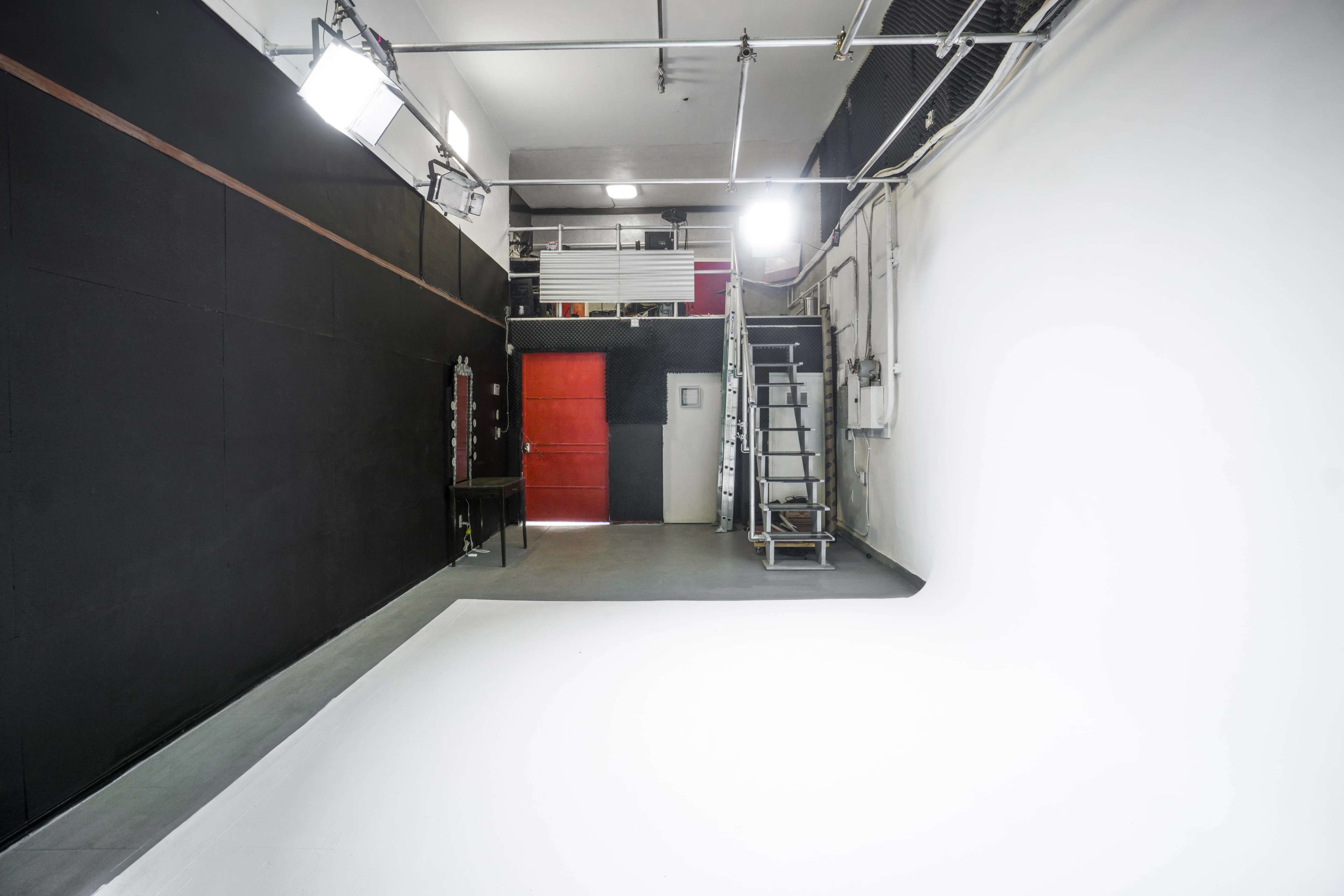 A spacious photography studio featuring a white background, black walls, and lighting equipment mounted overhead.