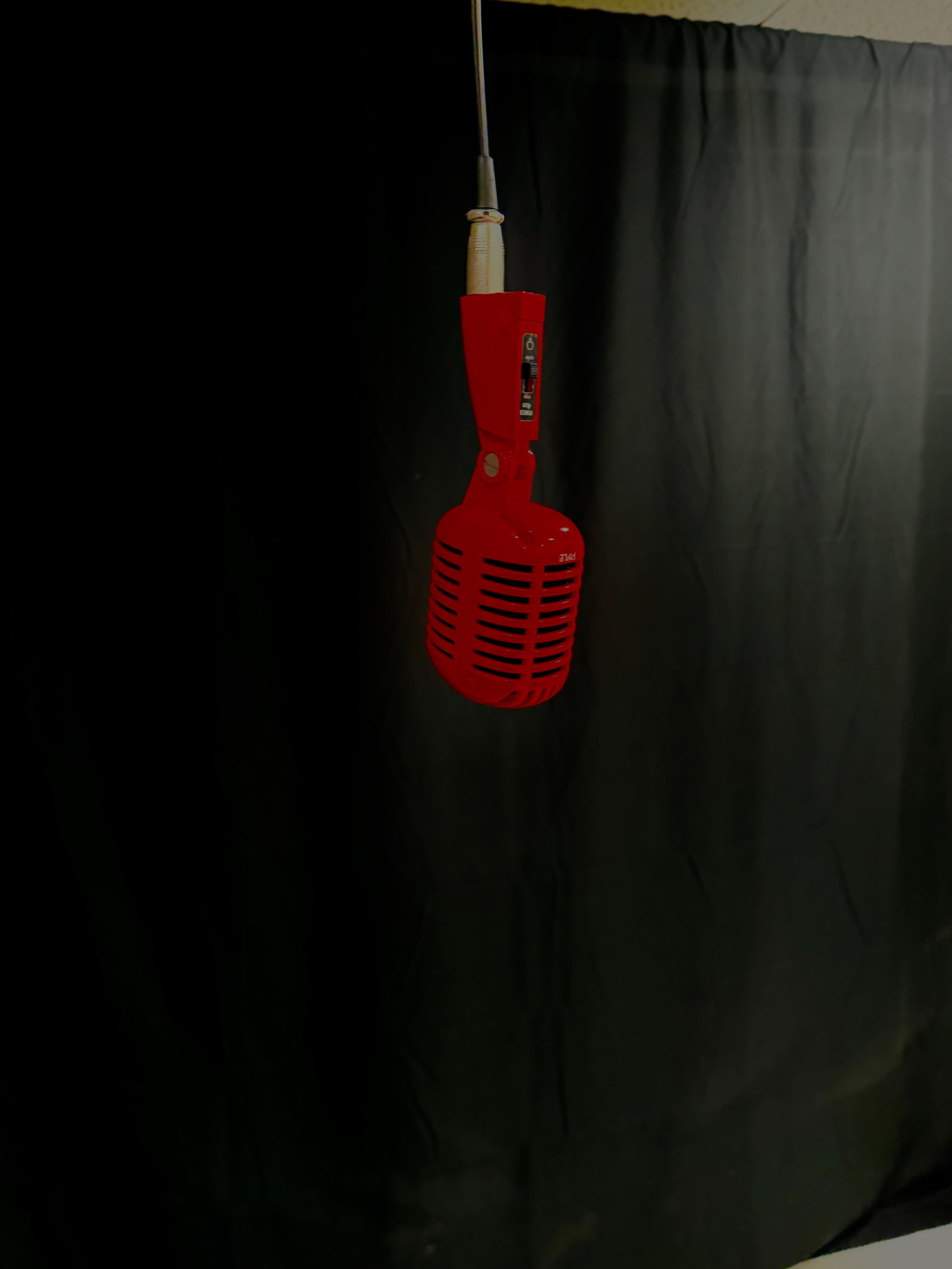 A vintage-style red microphone hangs from a cable against a black background.