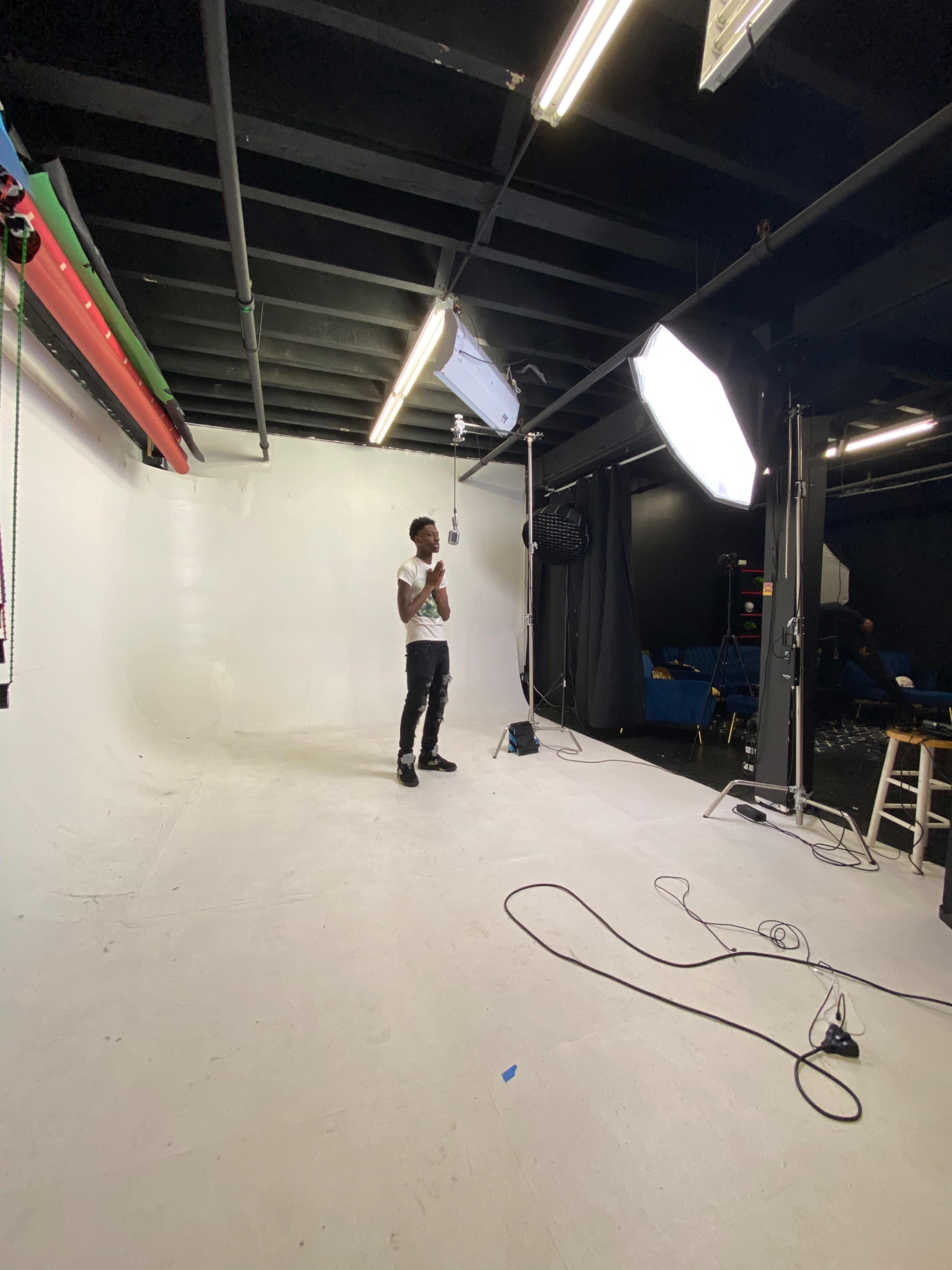 A person stands in a photography studio with a white backdrop and lighting equipment.