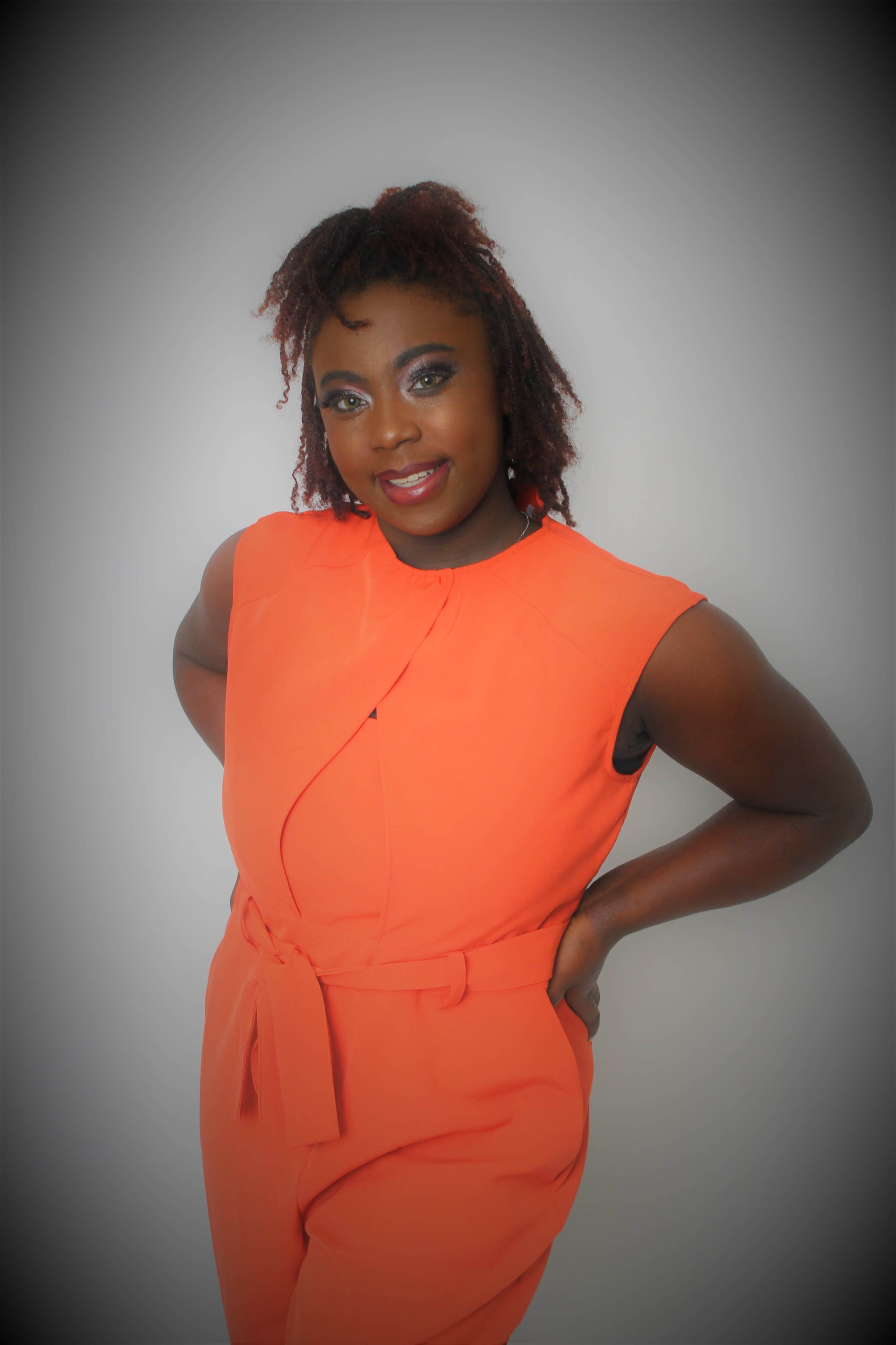 A person wearing an orange outfit poses in front of a neutral background.