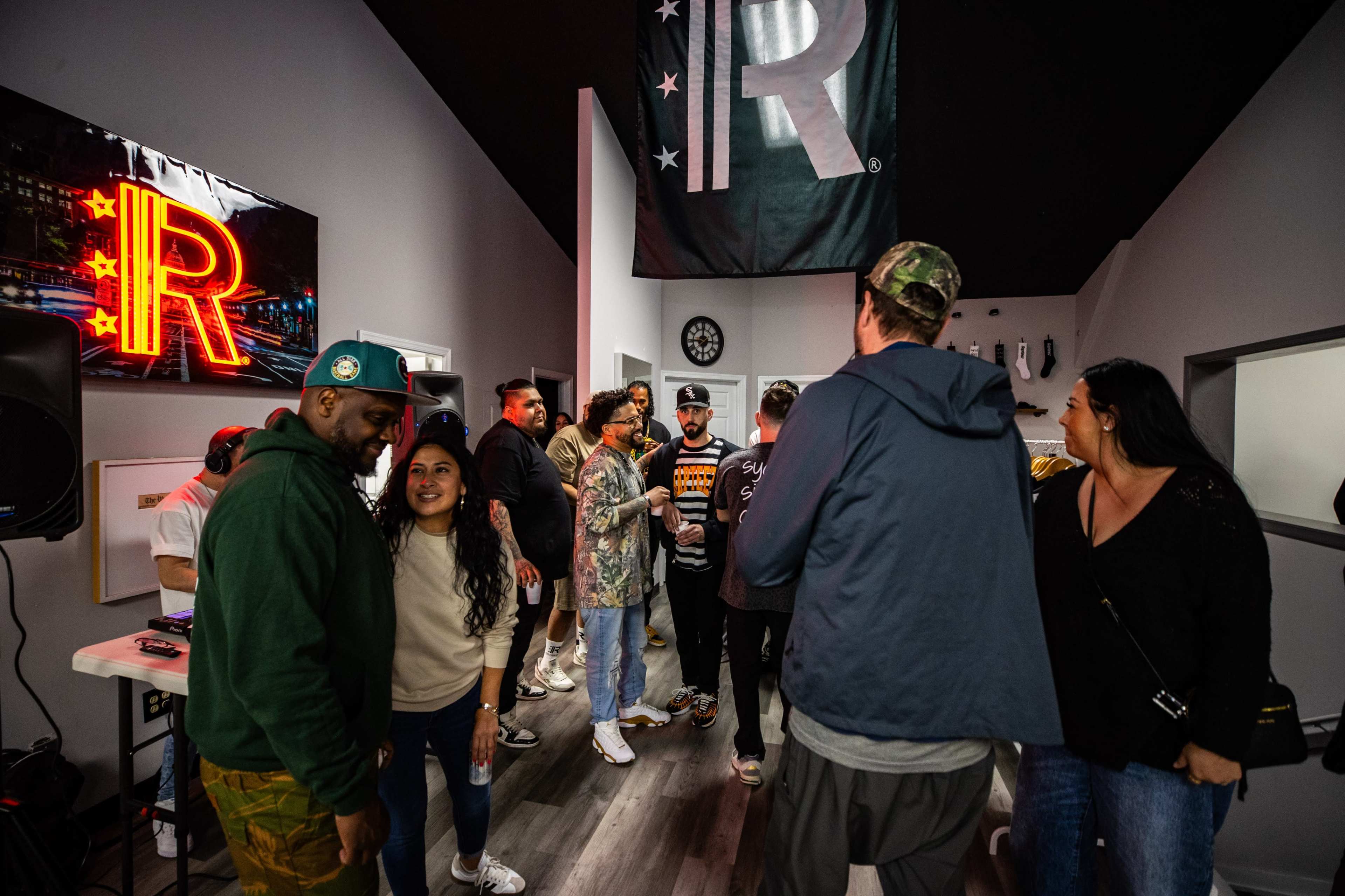 A group of people socialize in a modern room decorated with a large illuminated "R" and casual furnishings.