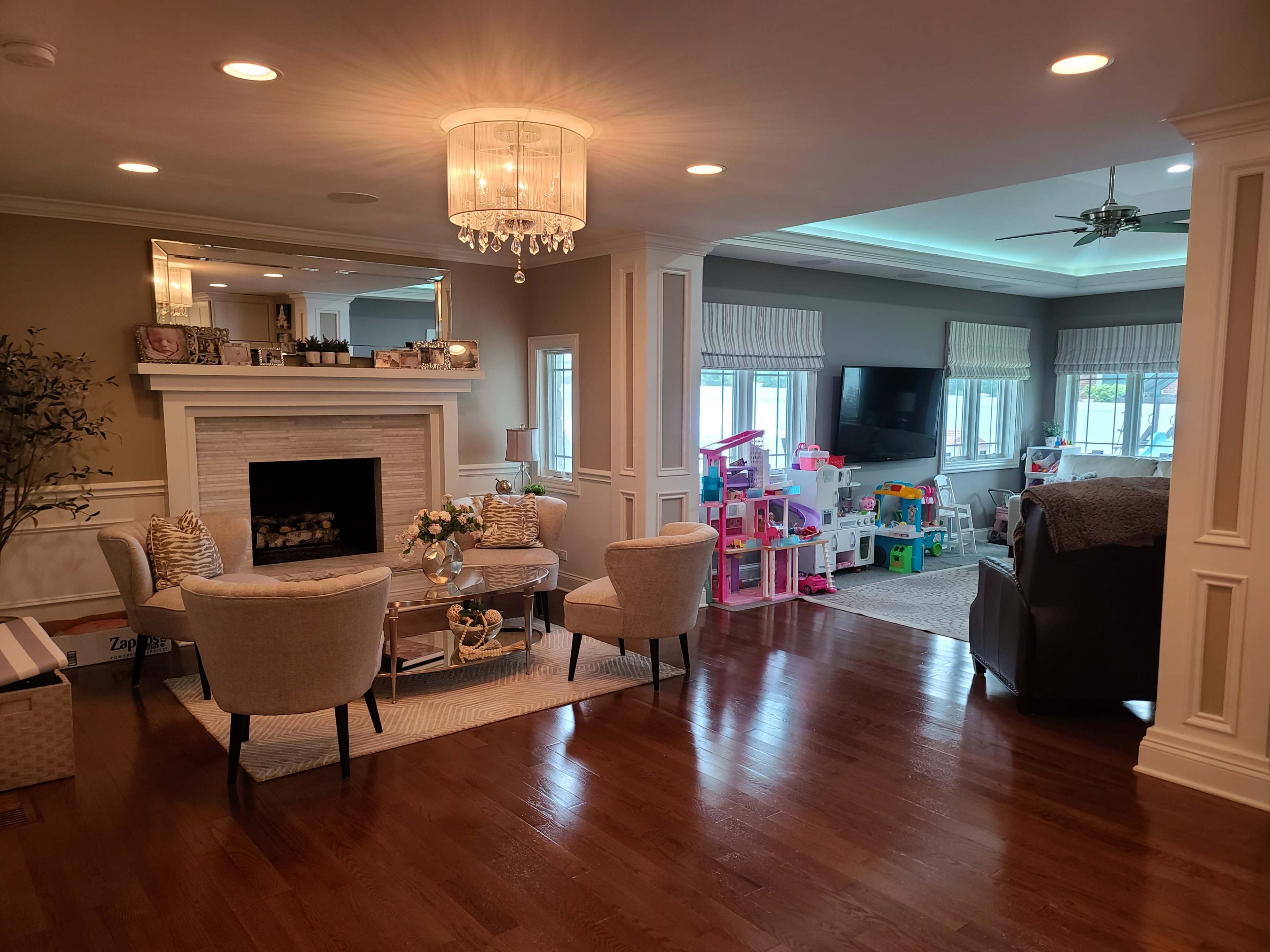 A living room featuring a fireplace, two armchairs with a small table between them, and a play area for children filled with toys.