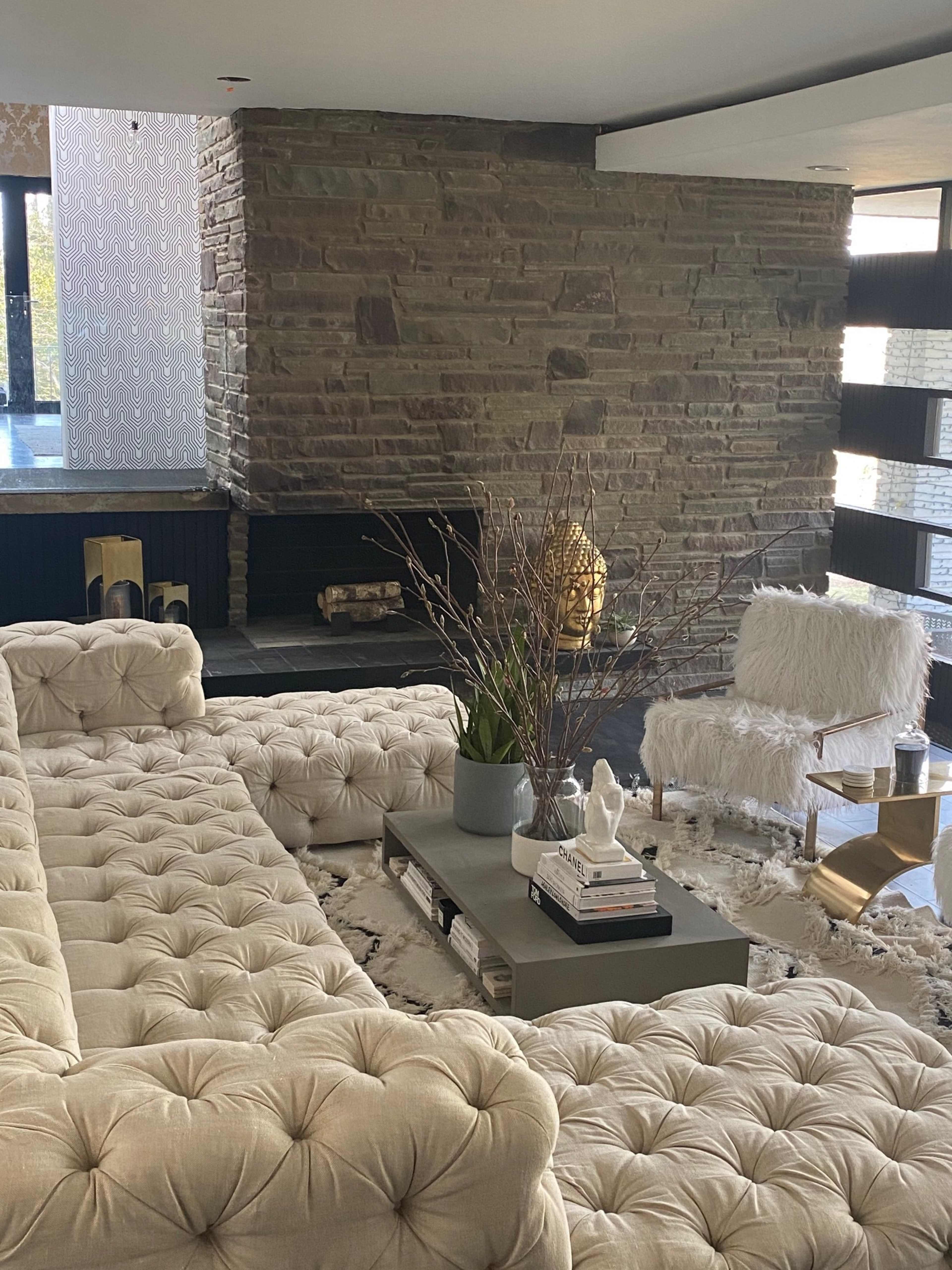 A modern living room featuring a tufted beige sofa, a stone accent wall, and a decorative coffee table with plants and books.