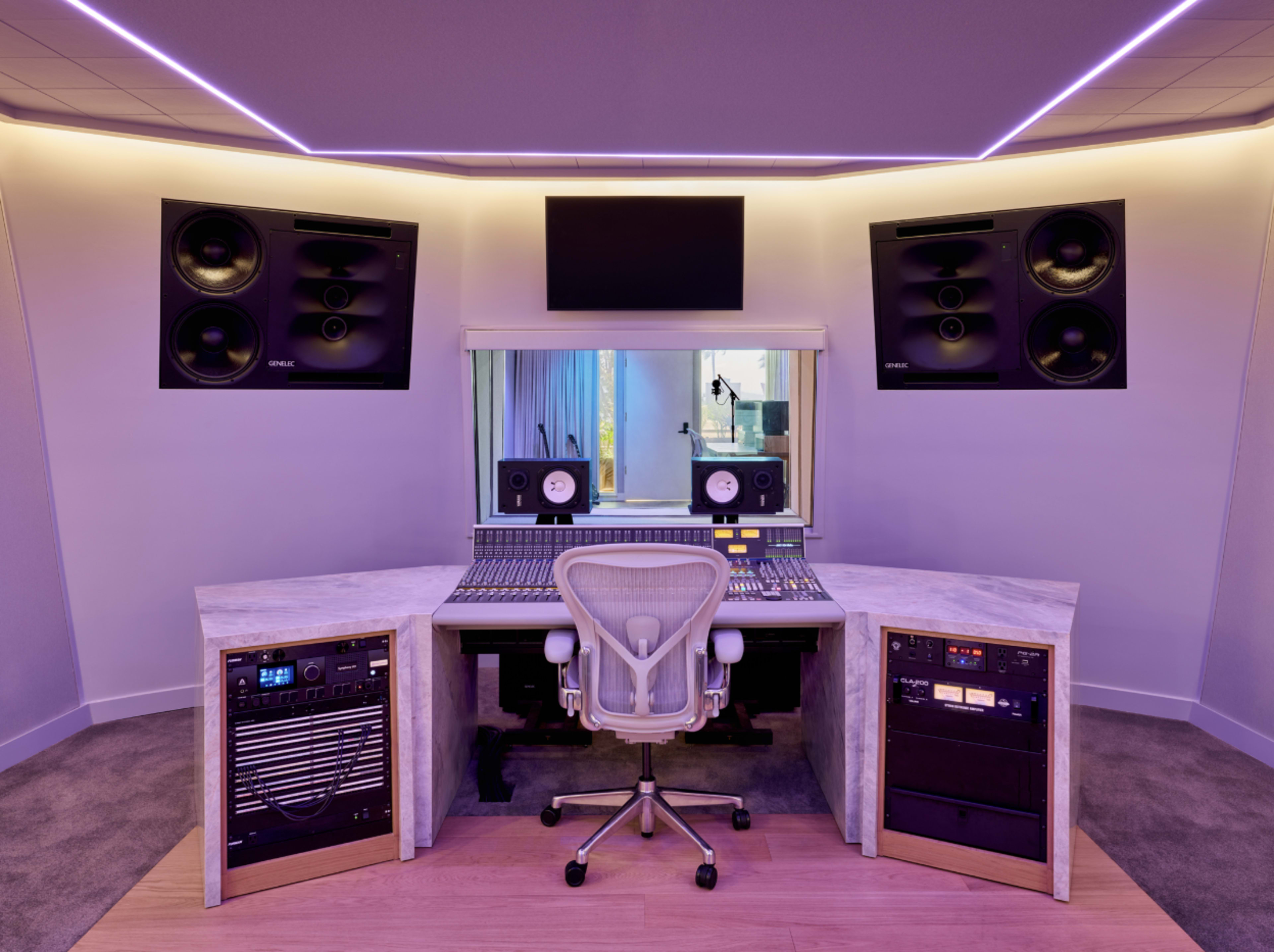 A modern music studio features a control desk with audio equipment, an ergonomic chair, and soundproofing elements along the walls.