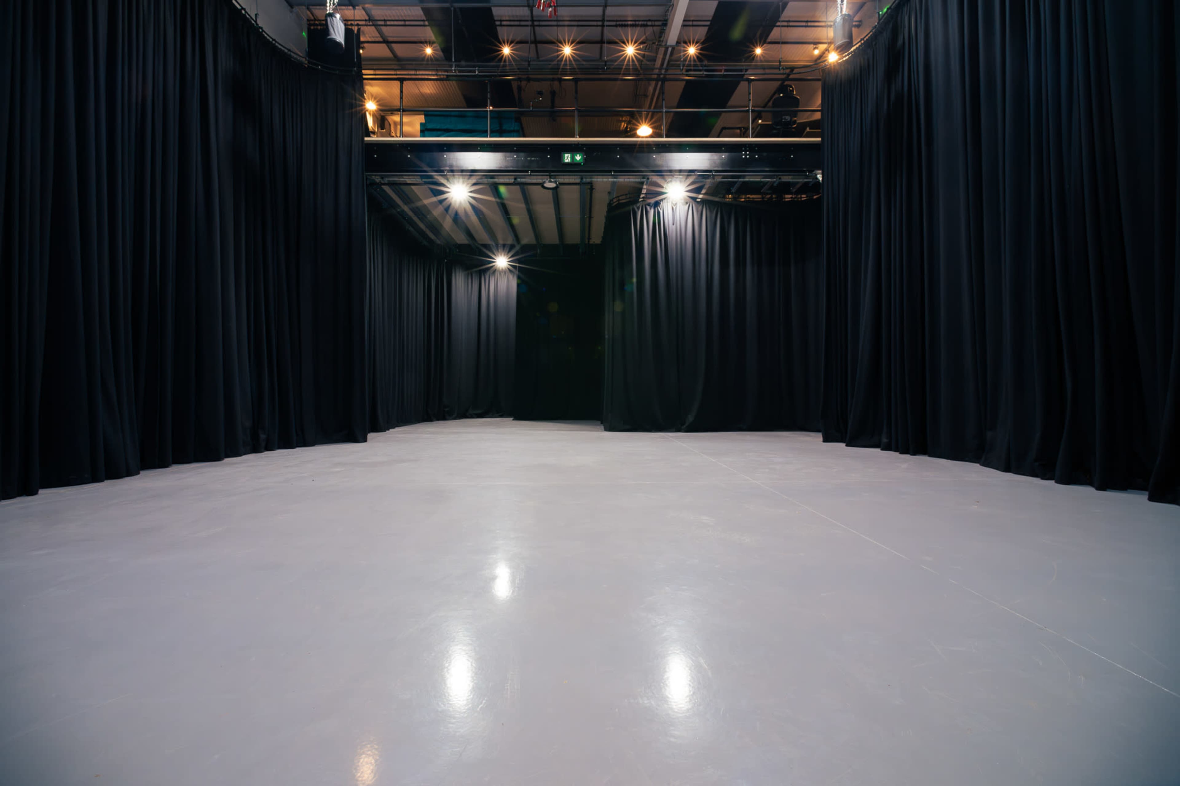 A spacious performance stage with black curtains and a polished gray floor, illuminated by overhead lights.