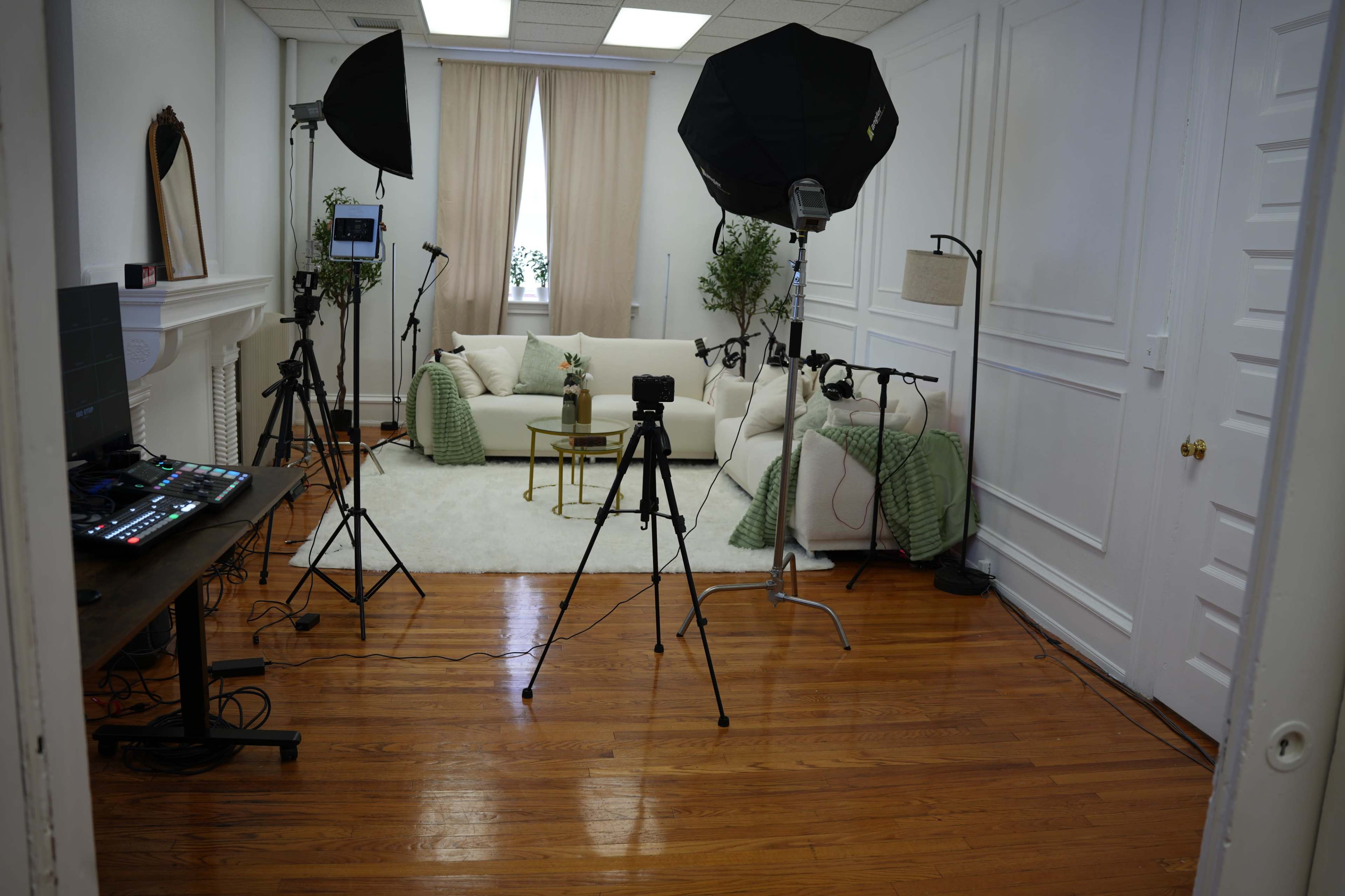 A well-lit studio setup featuring a sofa, decorative items, and multiple tripods with cameras and lighting equipment arranged around the room.