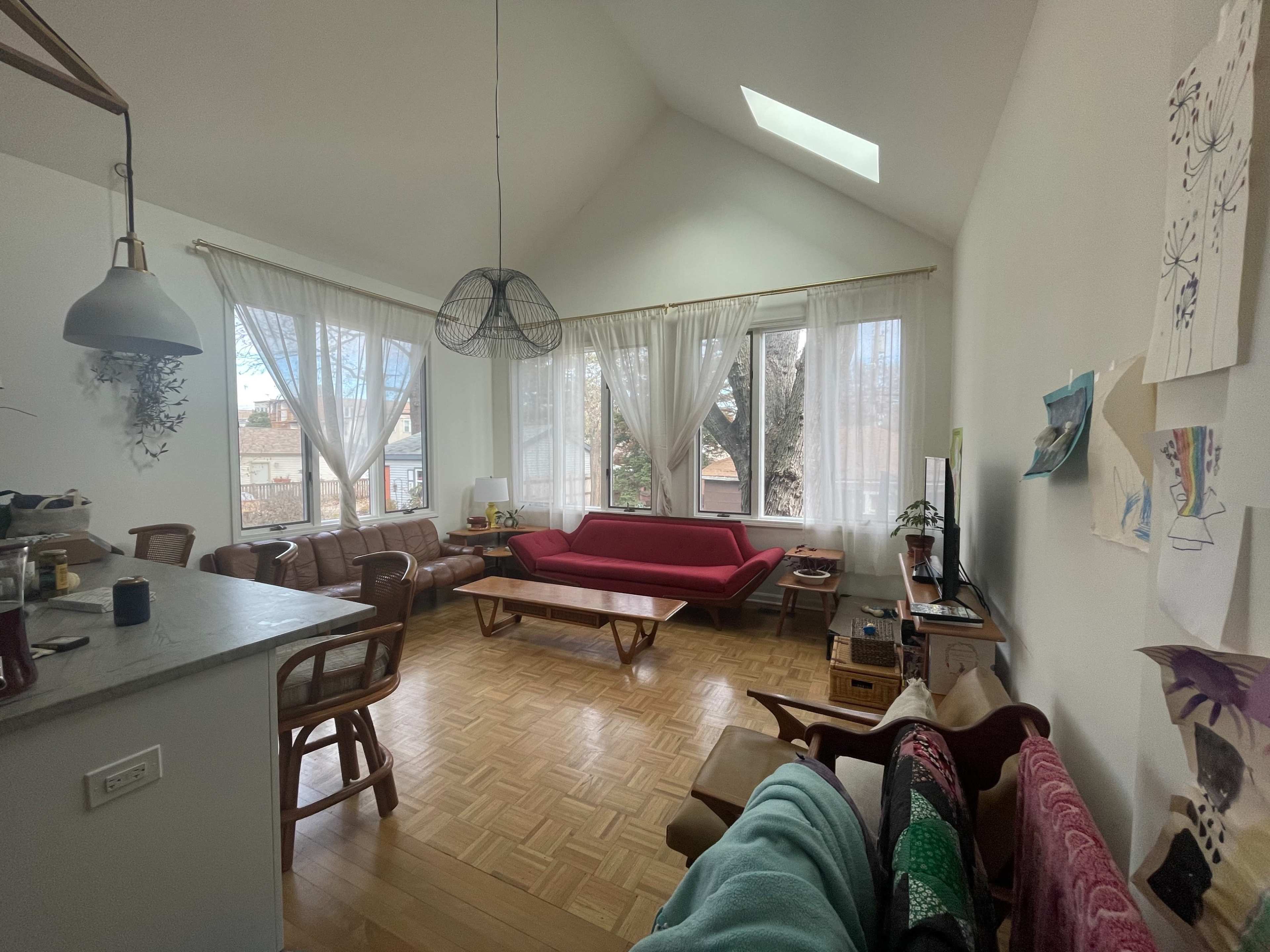 A spacious living room with large windows, a red sofa, wooden furniture, and a television.