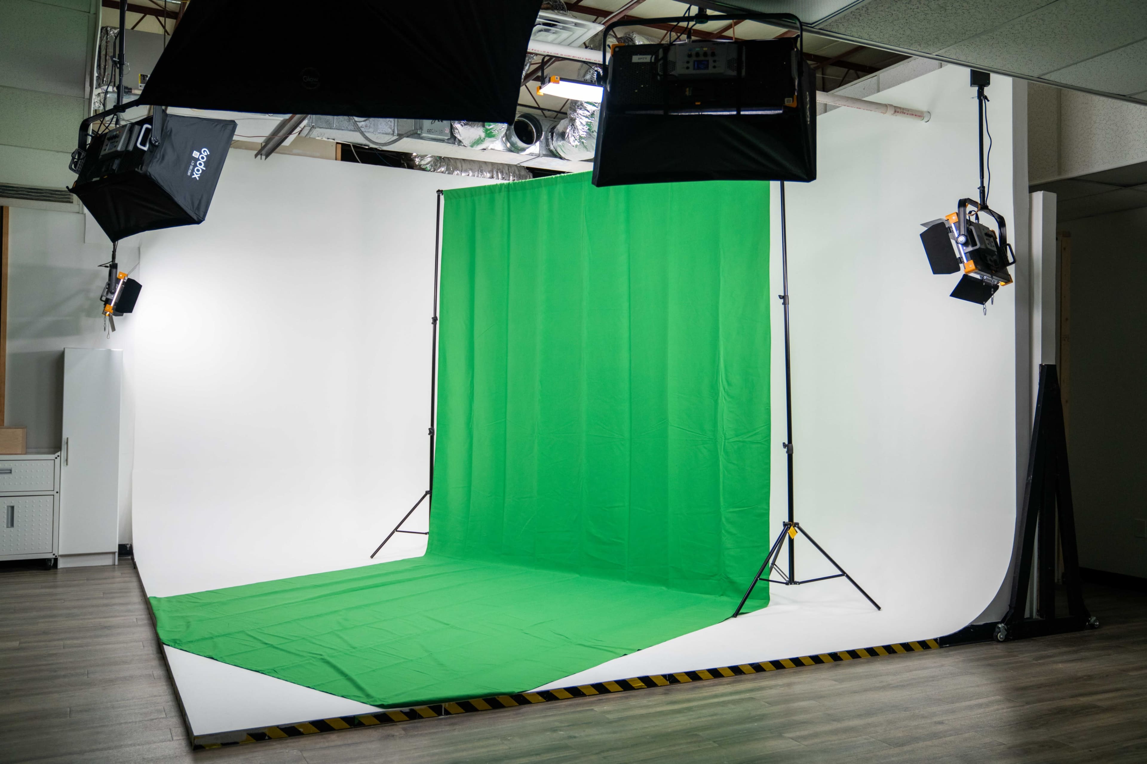 The image shows a photography studio featuring a green screen backdrop, illuminated by two lights on tripods.