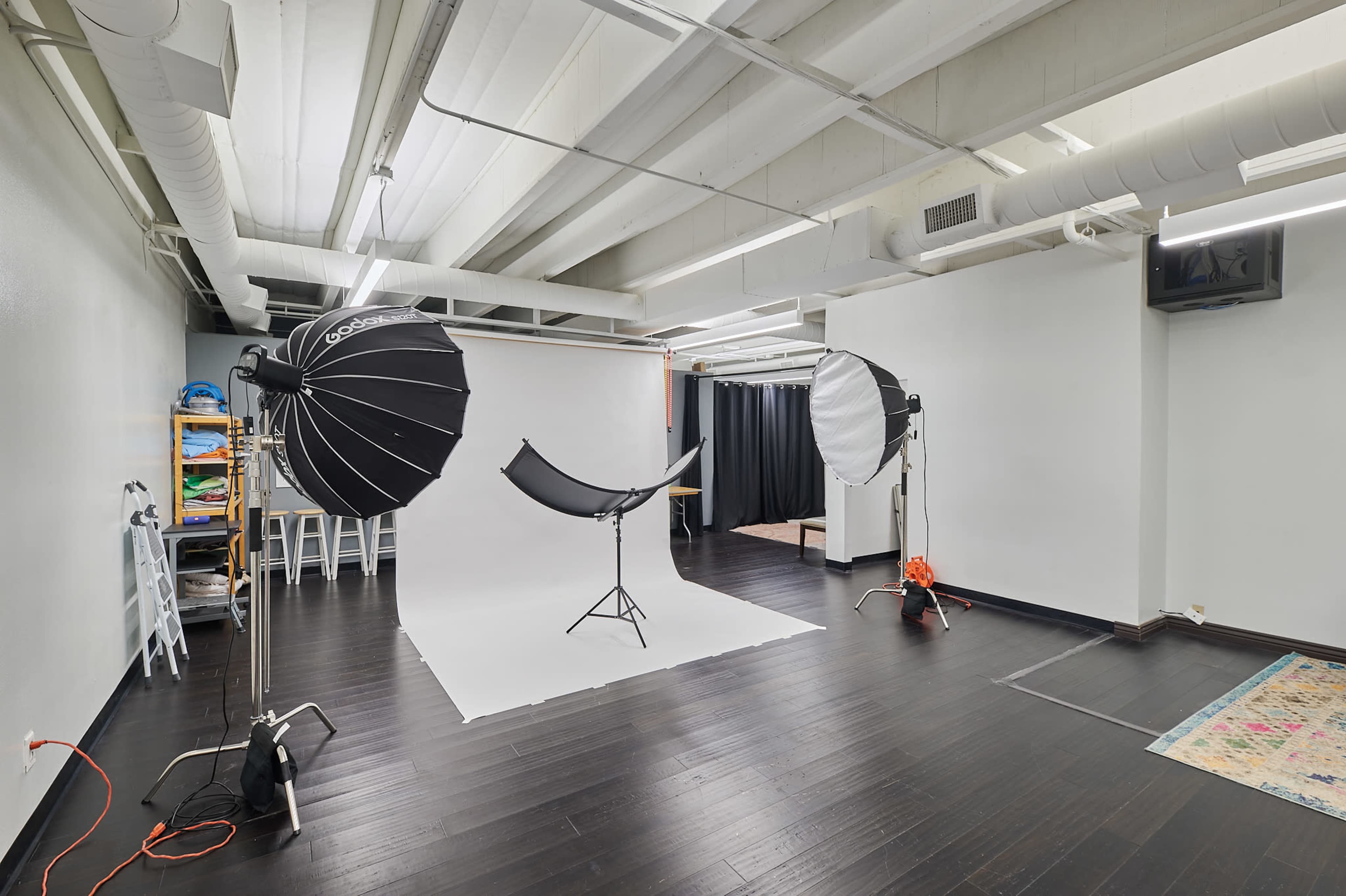 The image shows a photography studio equipped with lighting equipment, a backdrop, and a clean, open space on hardwood flooring.