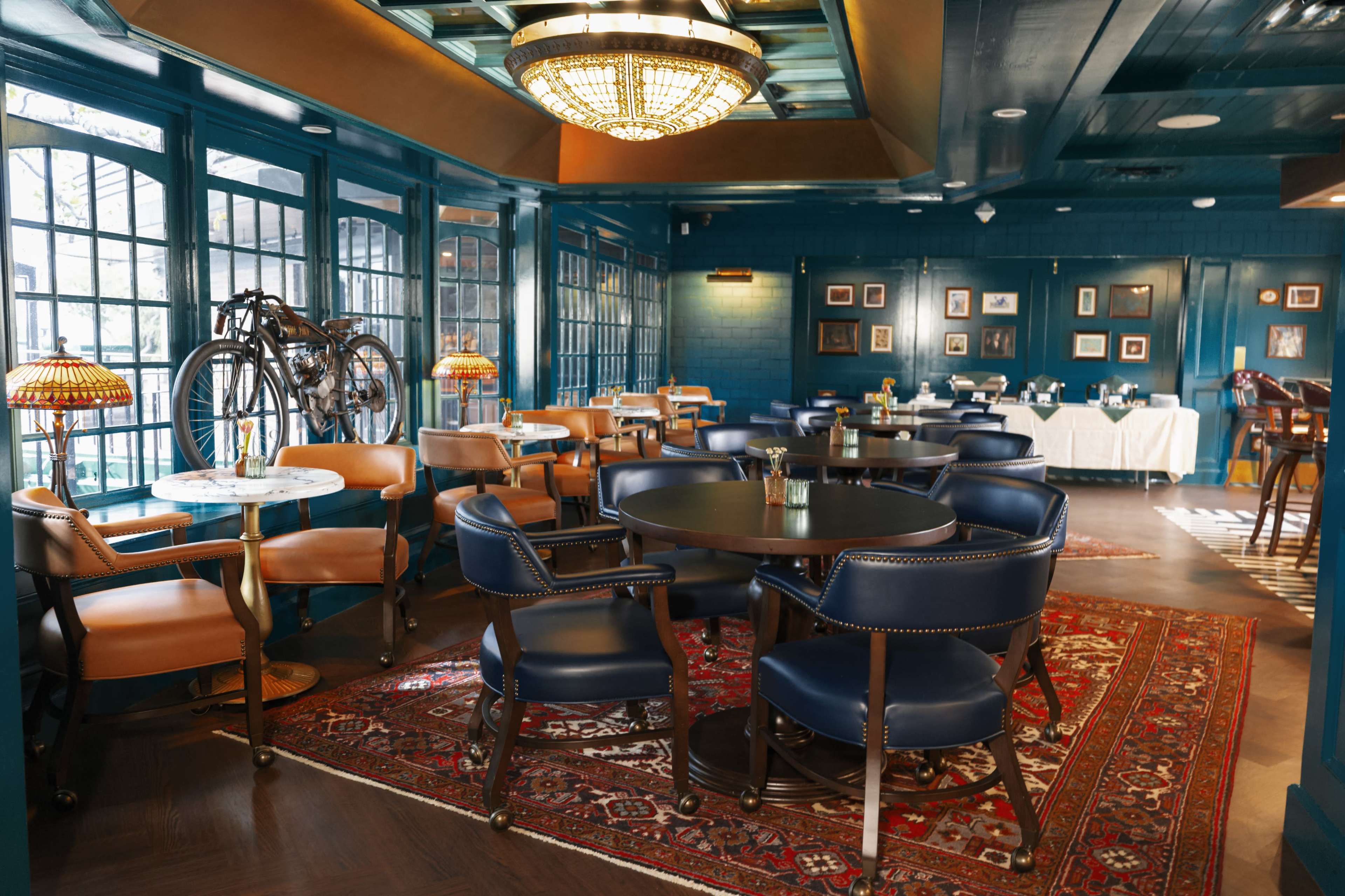 The image shows an upscale restaurant interior with dark blue walls, elegant wooden furniture, and a decorative bicycle mounted on the wall.