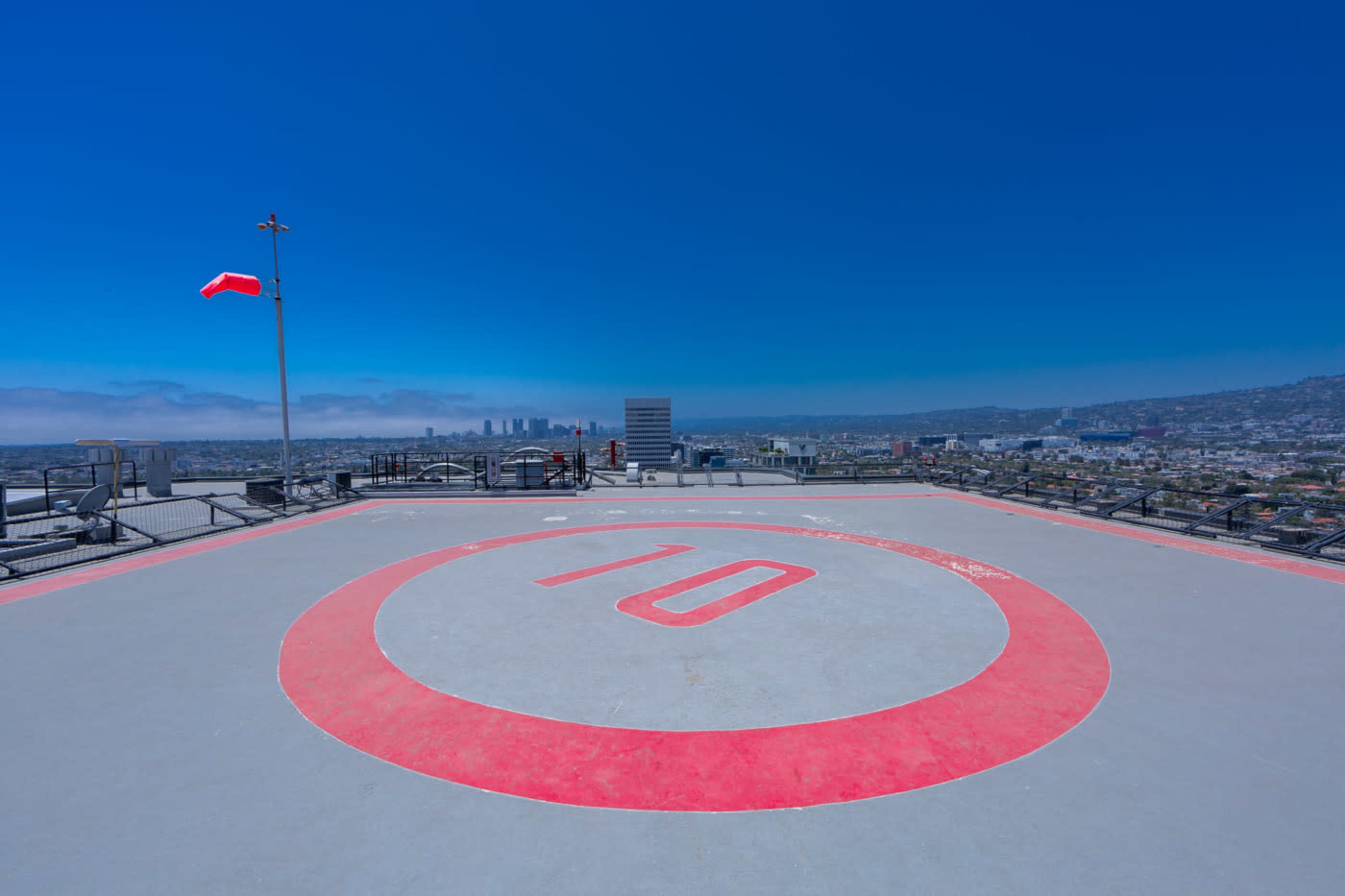 The image shows a large helicopter landing pad with the number "10" marked in red, overlooking a cityscape under a clear blue sky.