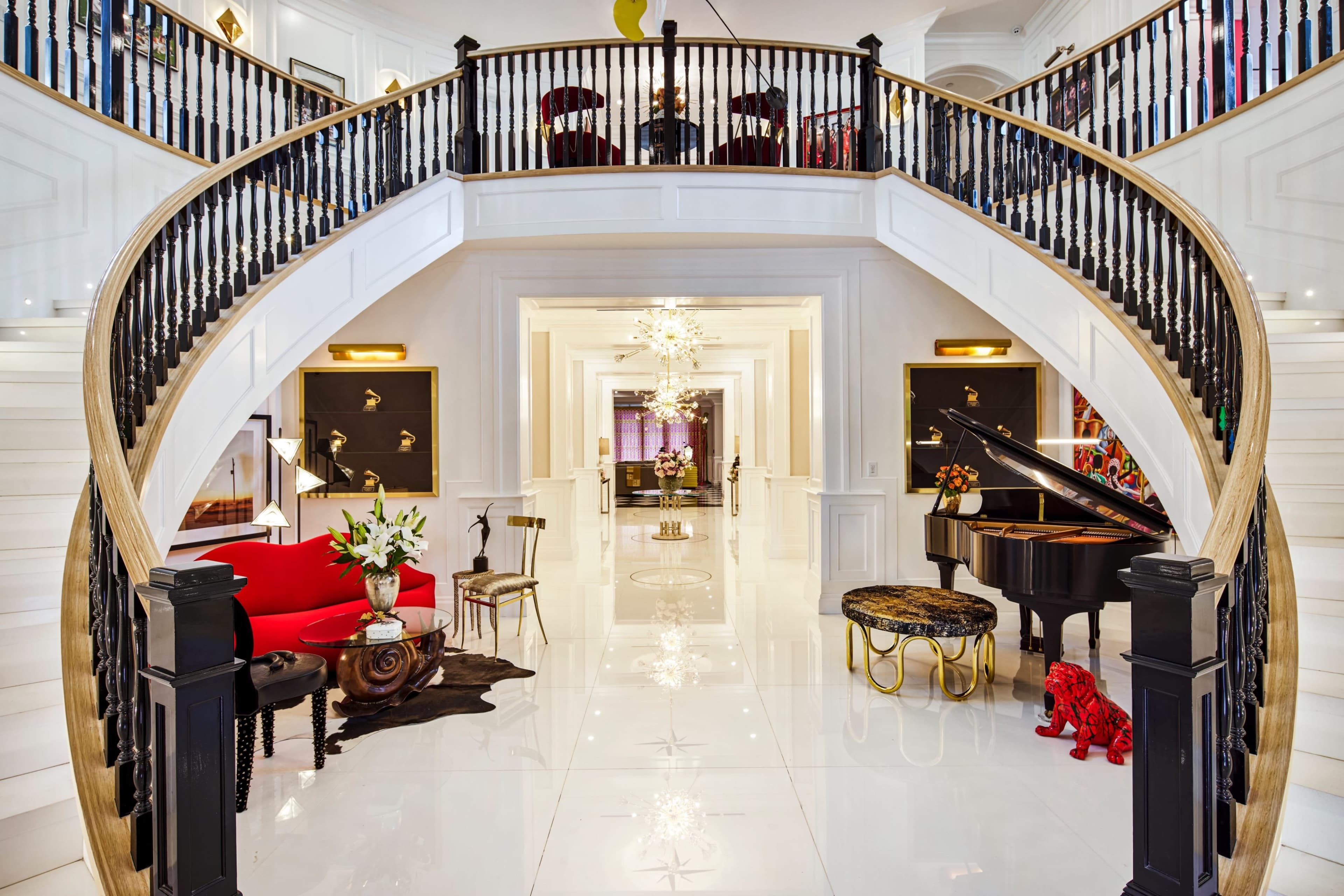 A spacious entryway featuring a grand staircase with a curved wooden banister, elegant furniture arrangements, and a piano.