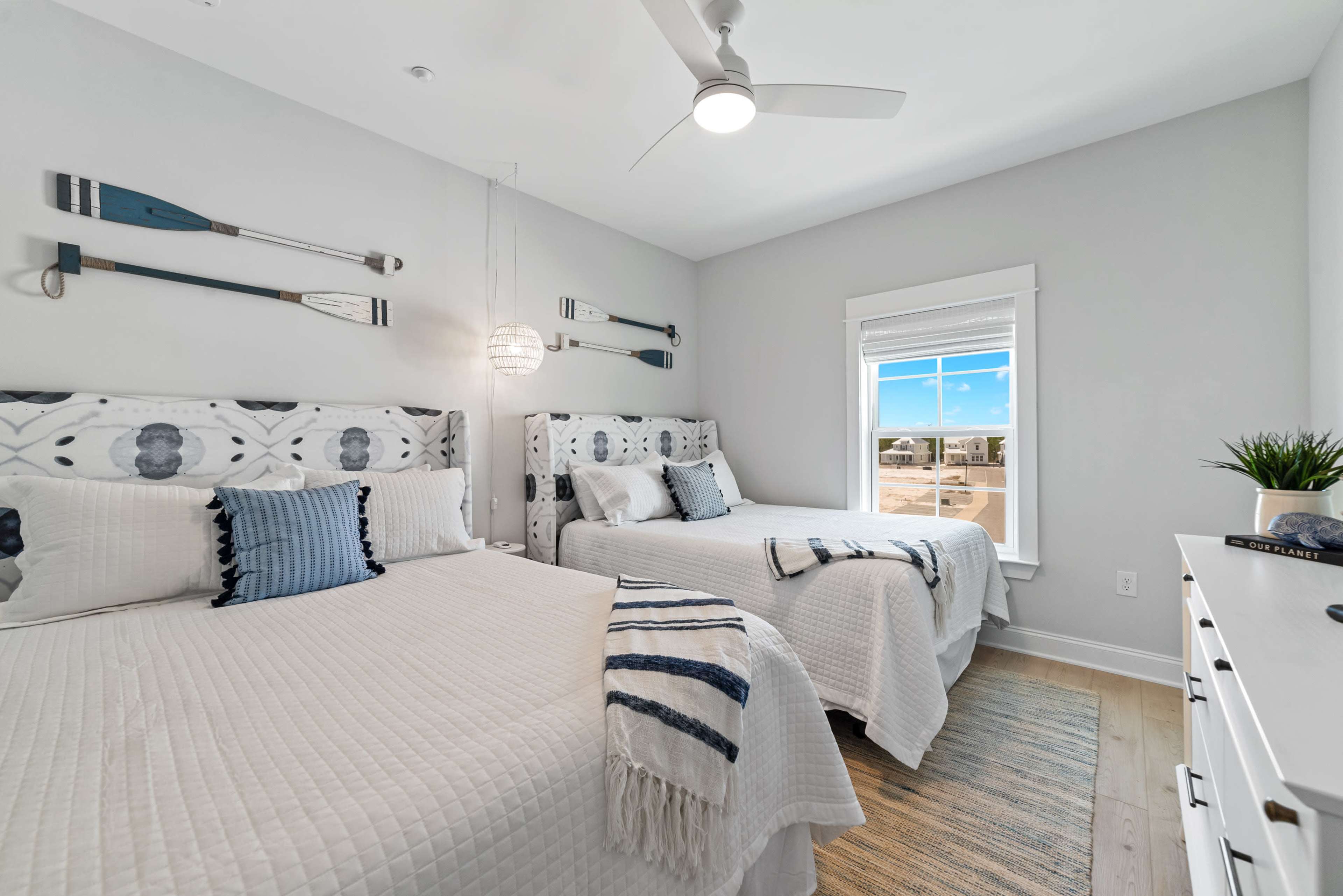 A well-decorated bedroom with two beds featuring patterned headboards, nautical-themed decor on the walls, and a window providing natural light.
