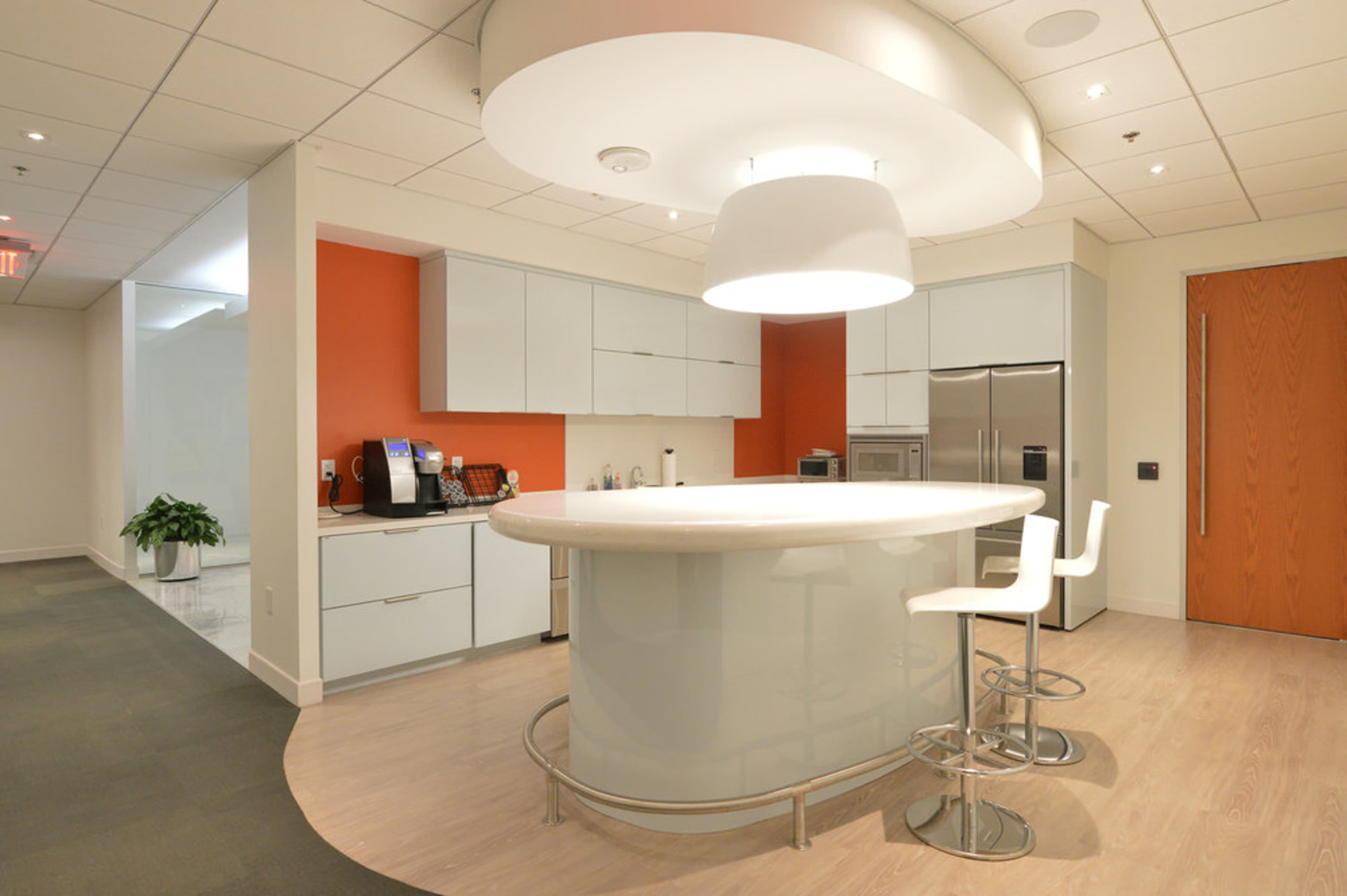 A modern kitchen features a curved white bar counter, sleek cabinetry, and stainless steel appliances.