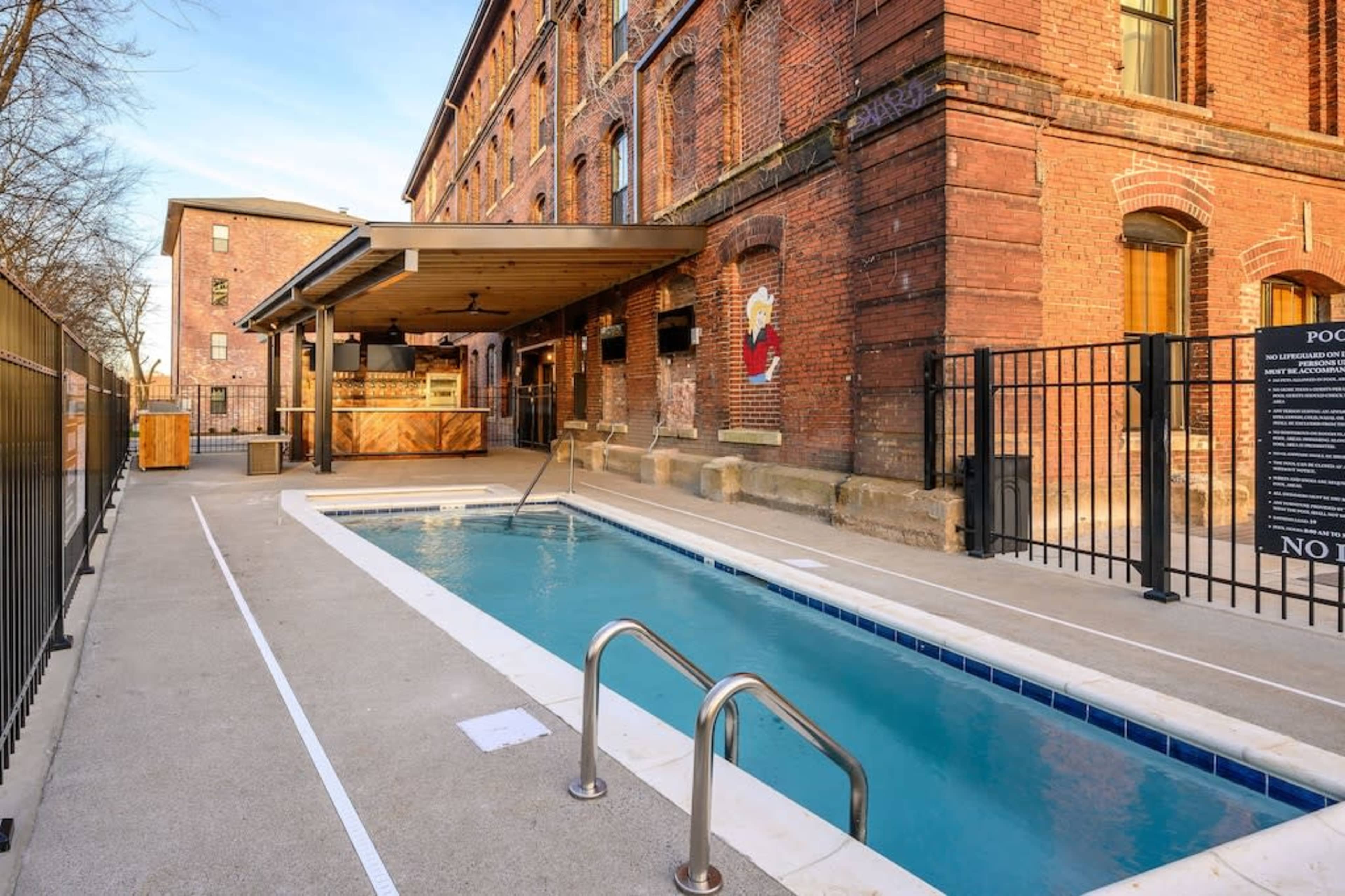 A narrow pool beside a brick building, with a wooden bar area and a fenced perimeter.