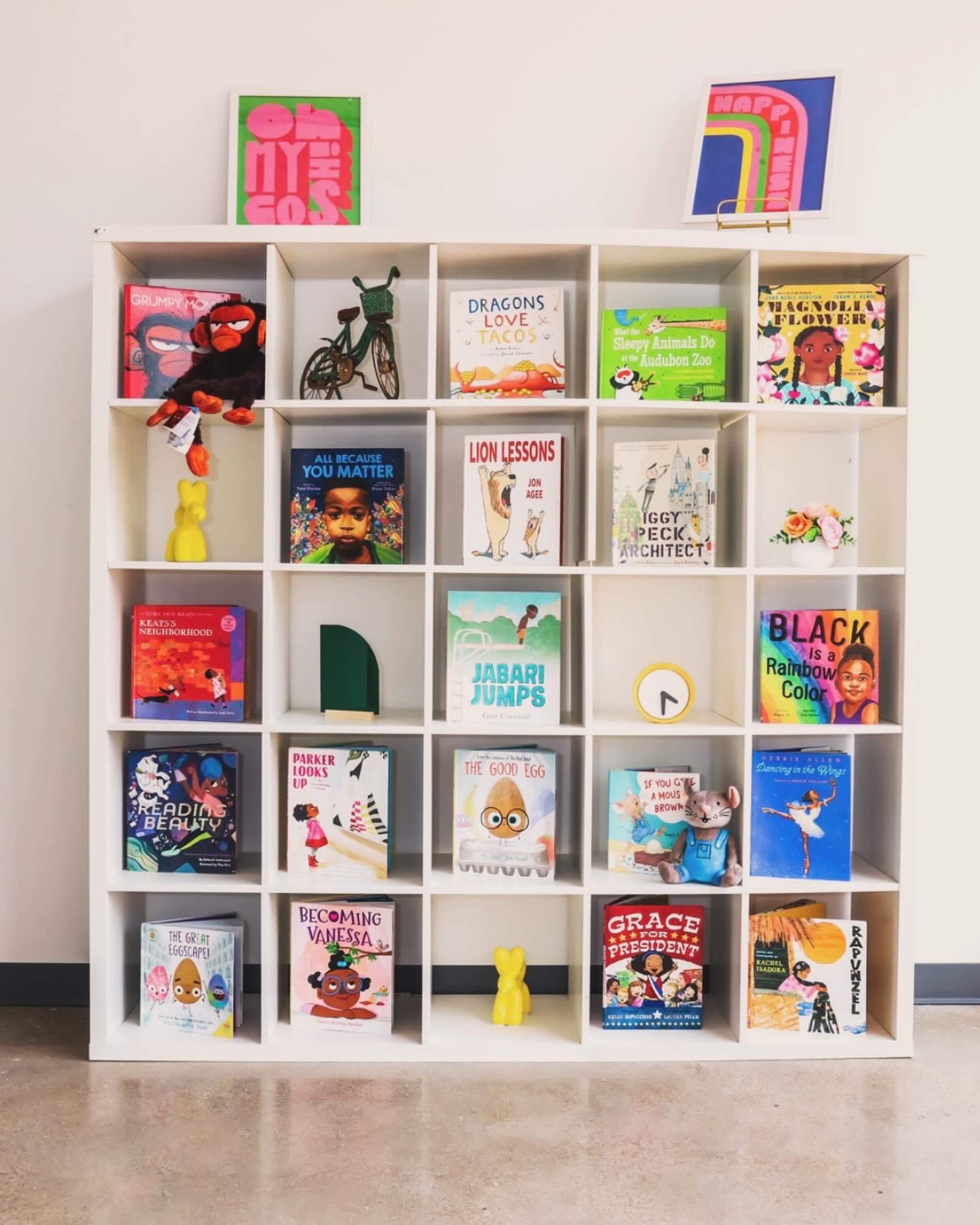 A white bookshelf filled with various children's books, with colorful book covers and decorative objects placed among them.
