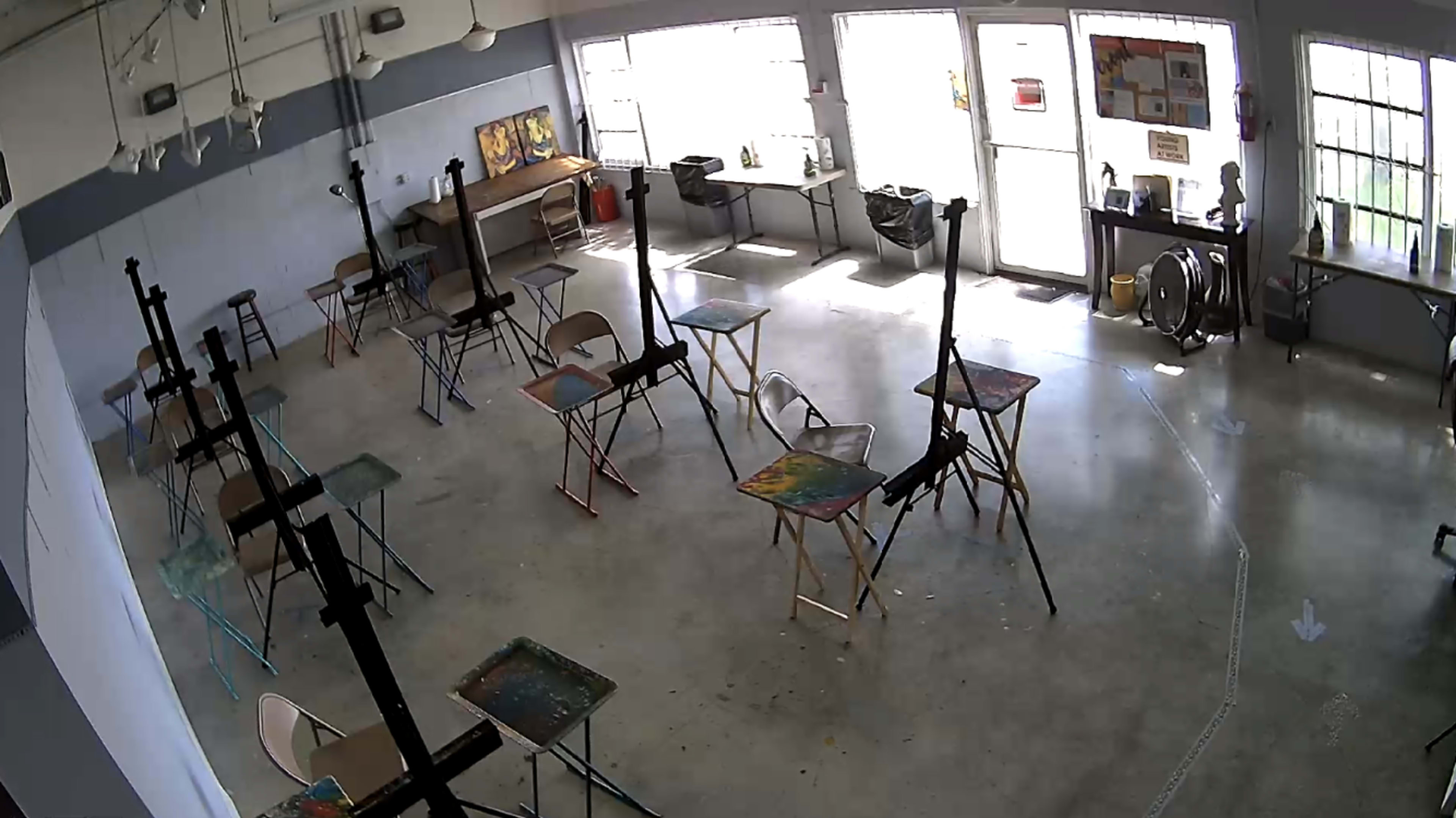 The image shows a spacious art studio with several easels and tables arranged in a well-lit room featuring large windows.