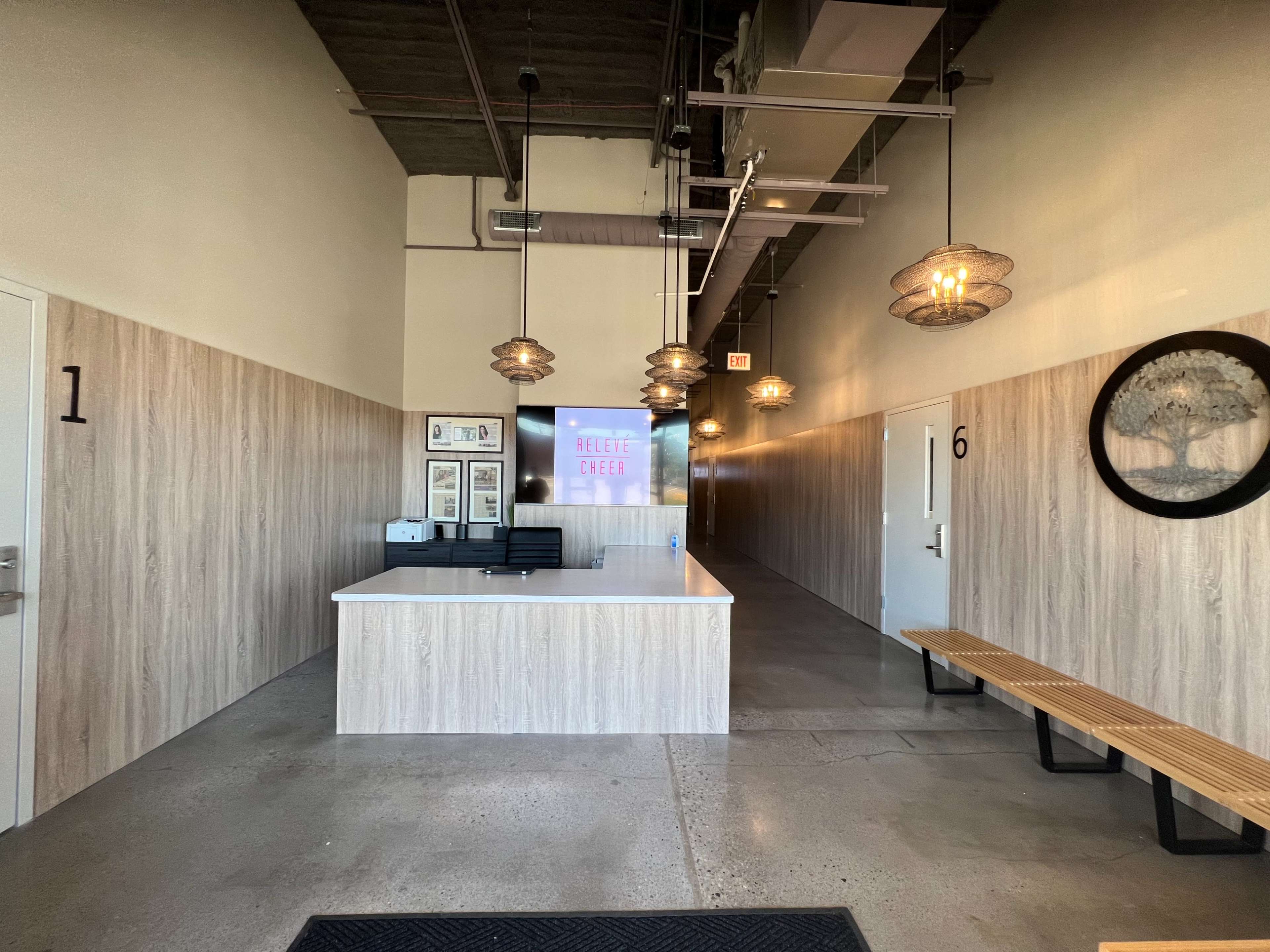 The image shows a reception area with a front desk, light fixtures, and a hallway leading to numbered rooms on one side.