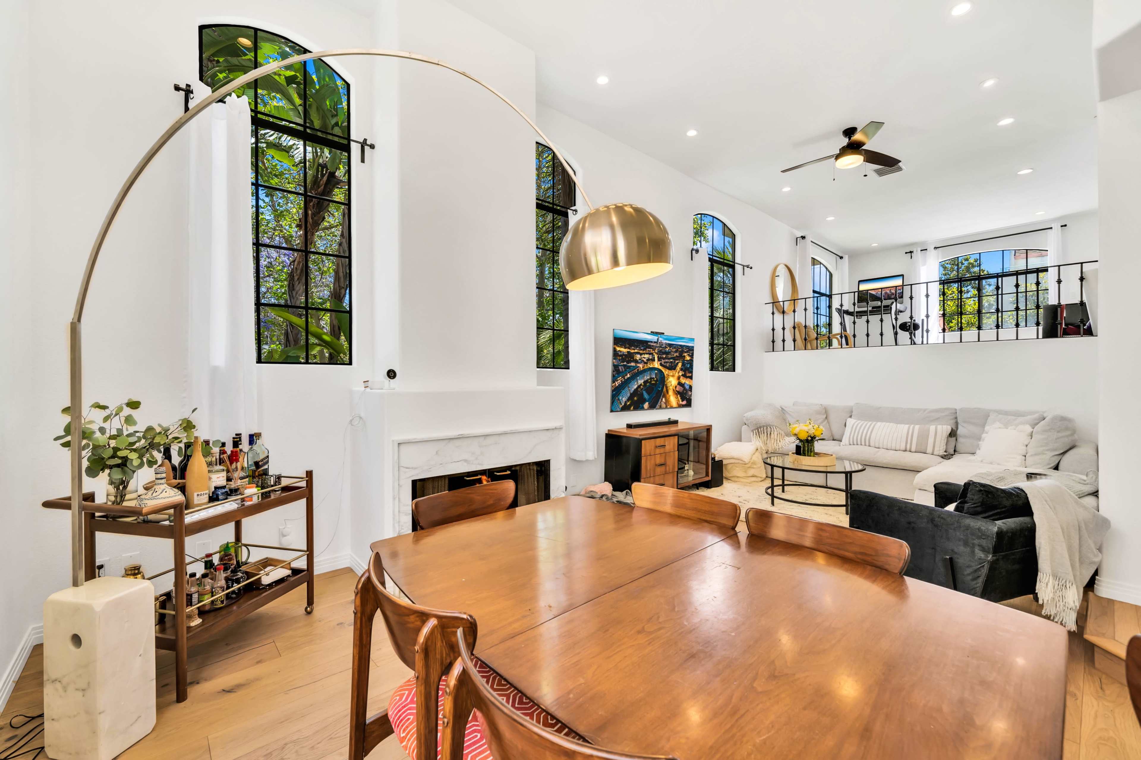 A modern living space with a dining area, a large sectional sofa, and large windows that allow natural light to enter.