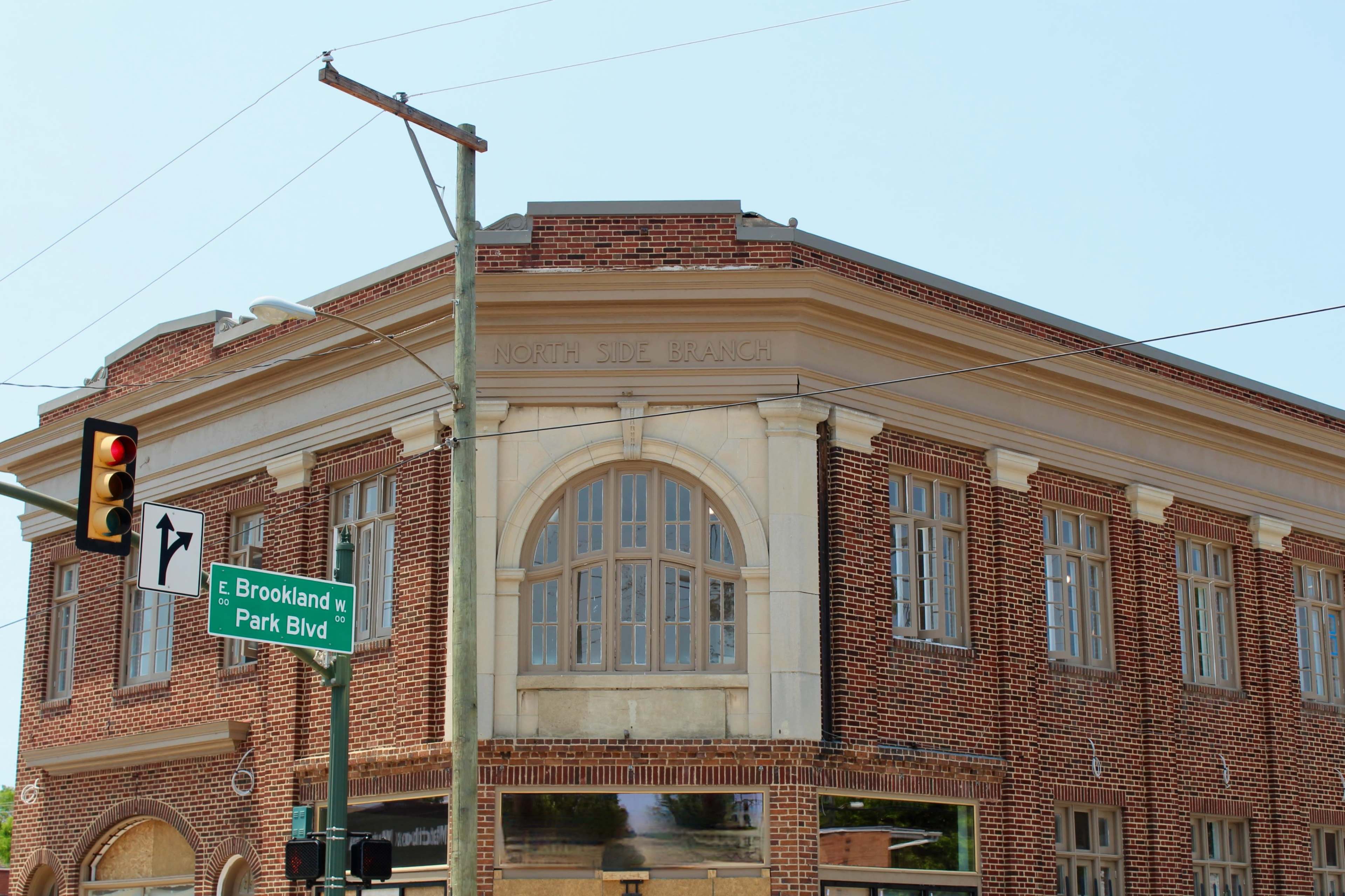 The image shows a historic brick building with a large arched window, labeled "North Side Branch," located at a street intersection with traffic lights and a street sign for Park Boulevard and Brookland.
