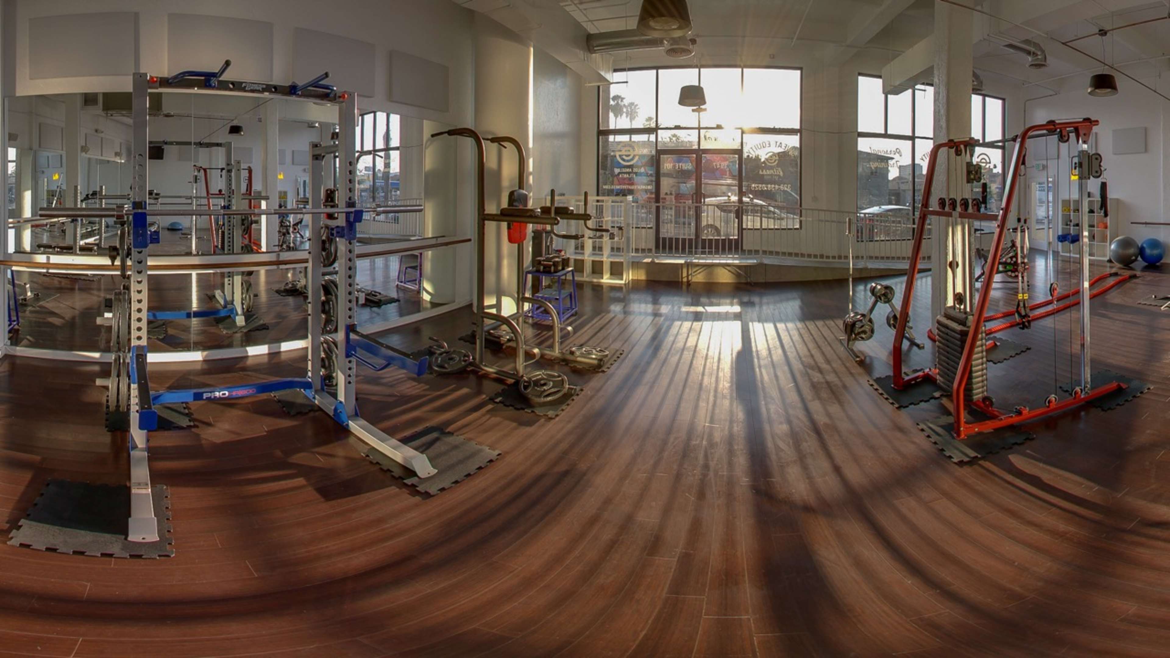 A spacious gym interior with various exercise equipment arranged on polished wooden floors.
