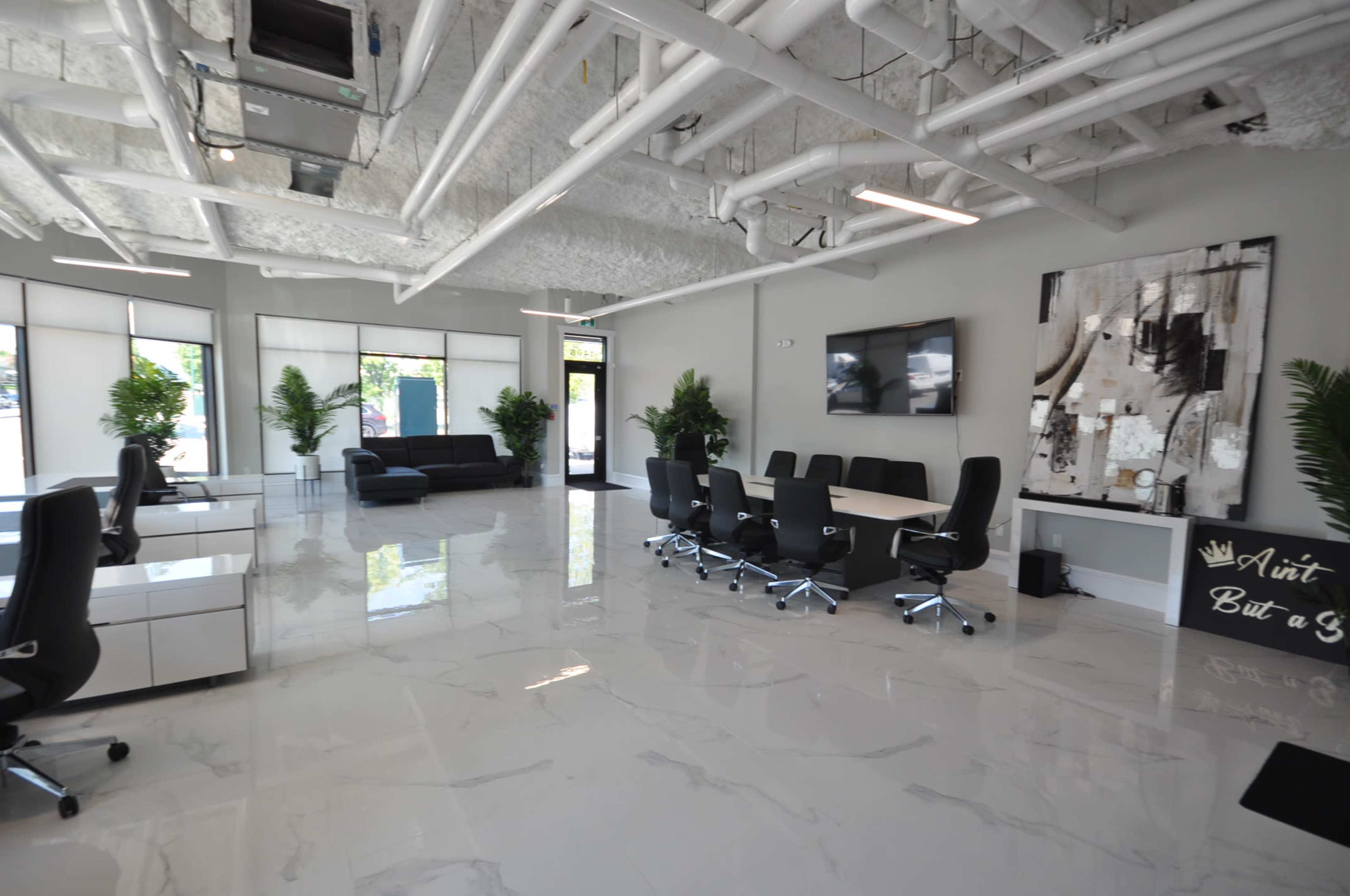 A modern, spacious office with white walls, glossy tile flooring, a conference table, and desks arranged in a bright, well-lit environment.