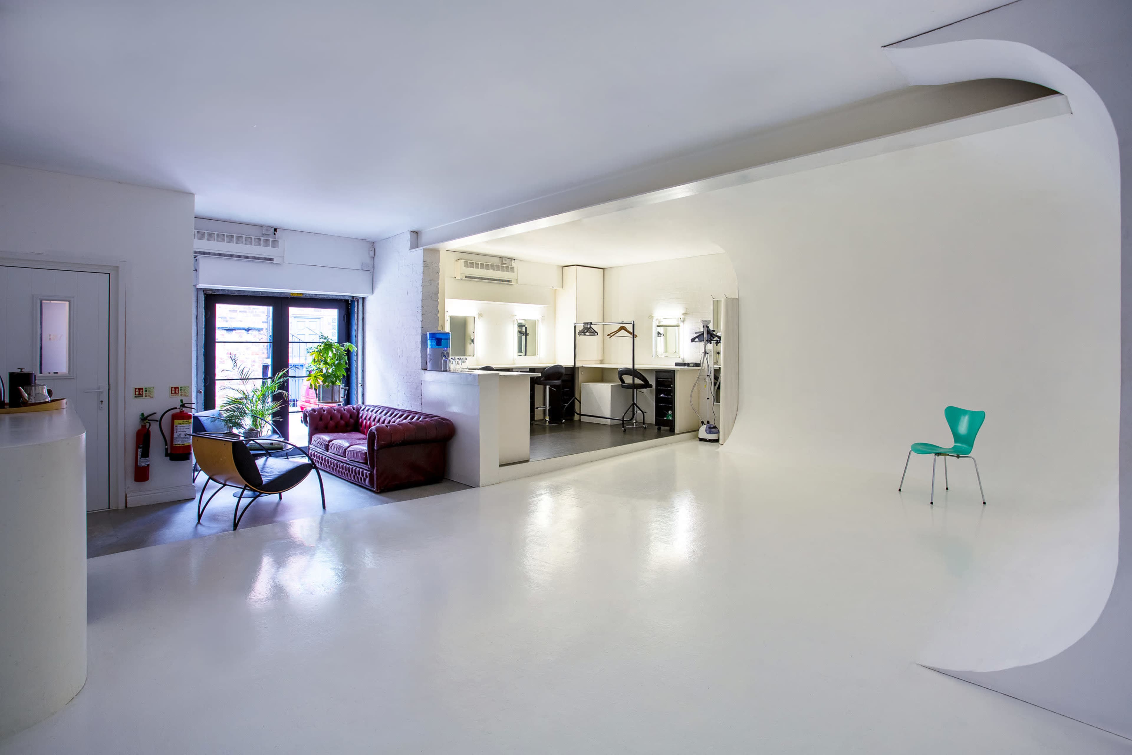 A modern, open-concept living space featuring a red sofa, a sleek kitchen area, and a single green chair against a white backdrop.