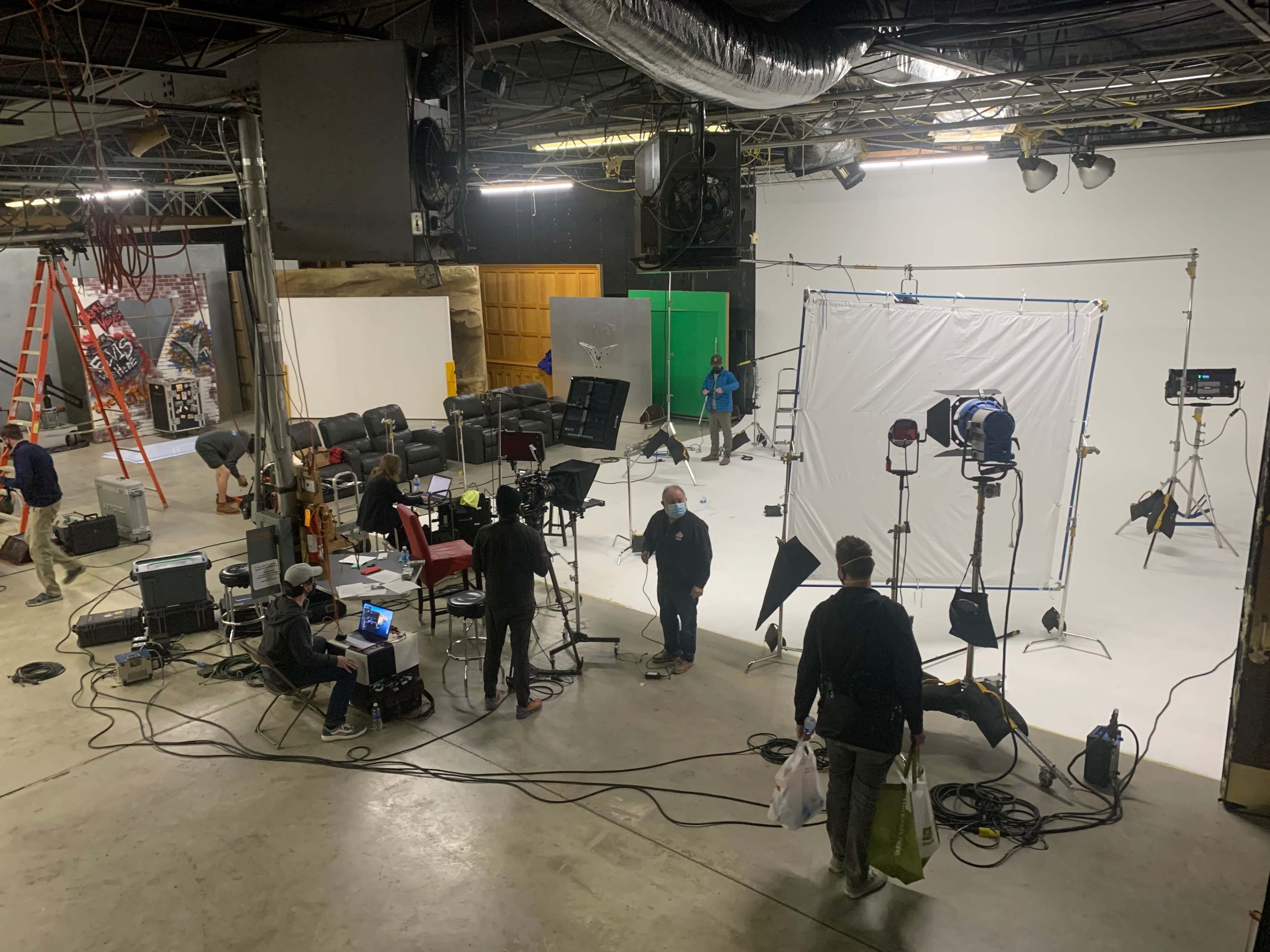 A film crew sets up equipment in a spacious studio with various backdrops and lighting setups.