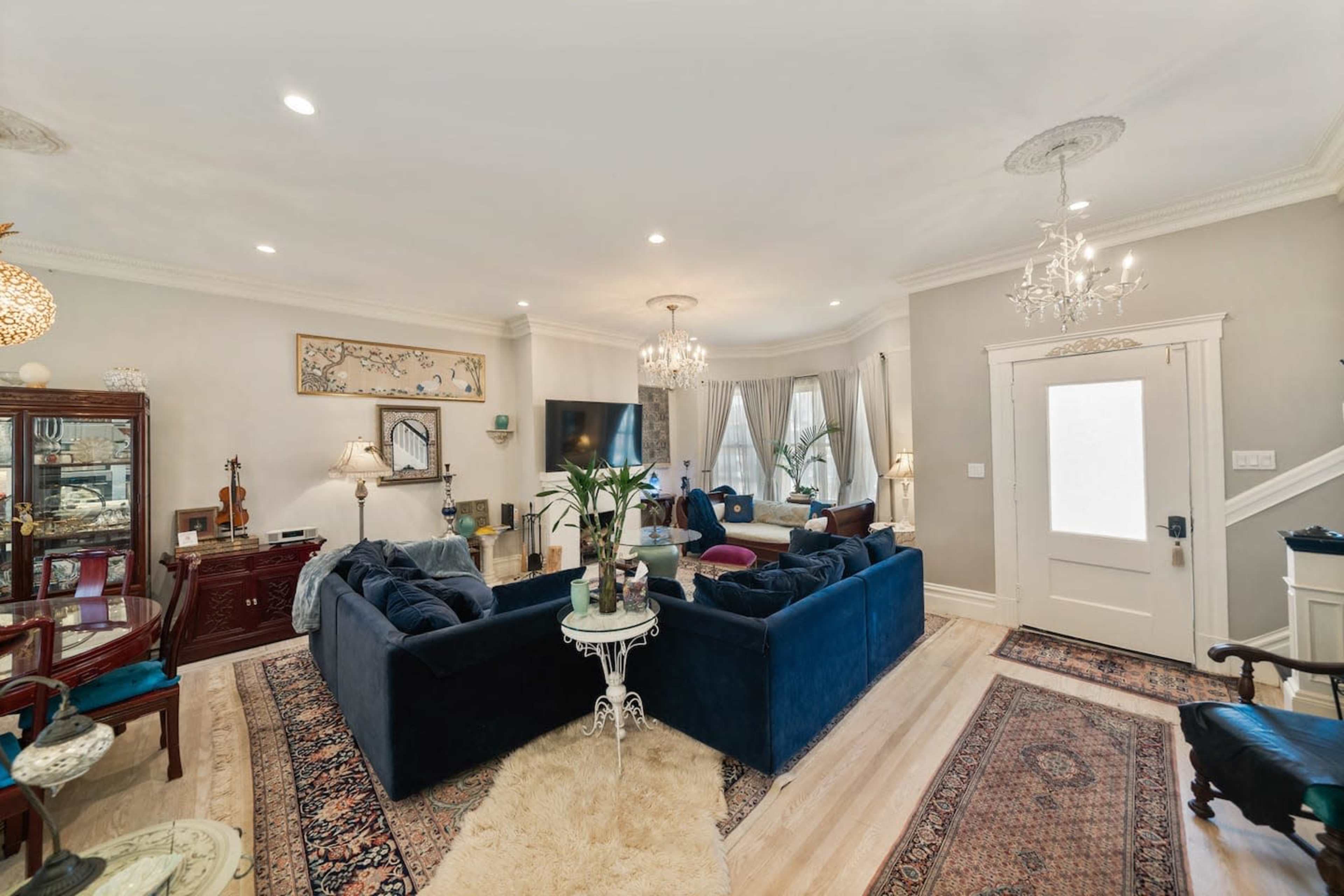 A spacious living room with two sofas arranged around a central coffee table, decorative chandeliers, and a mix of traditional and modern furniture.