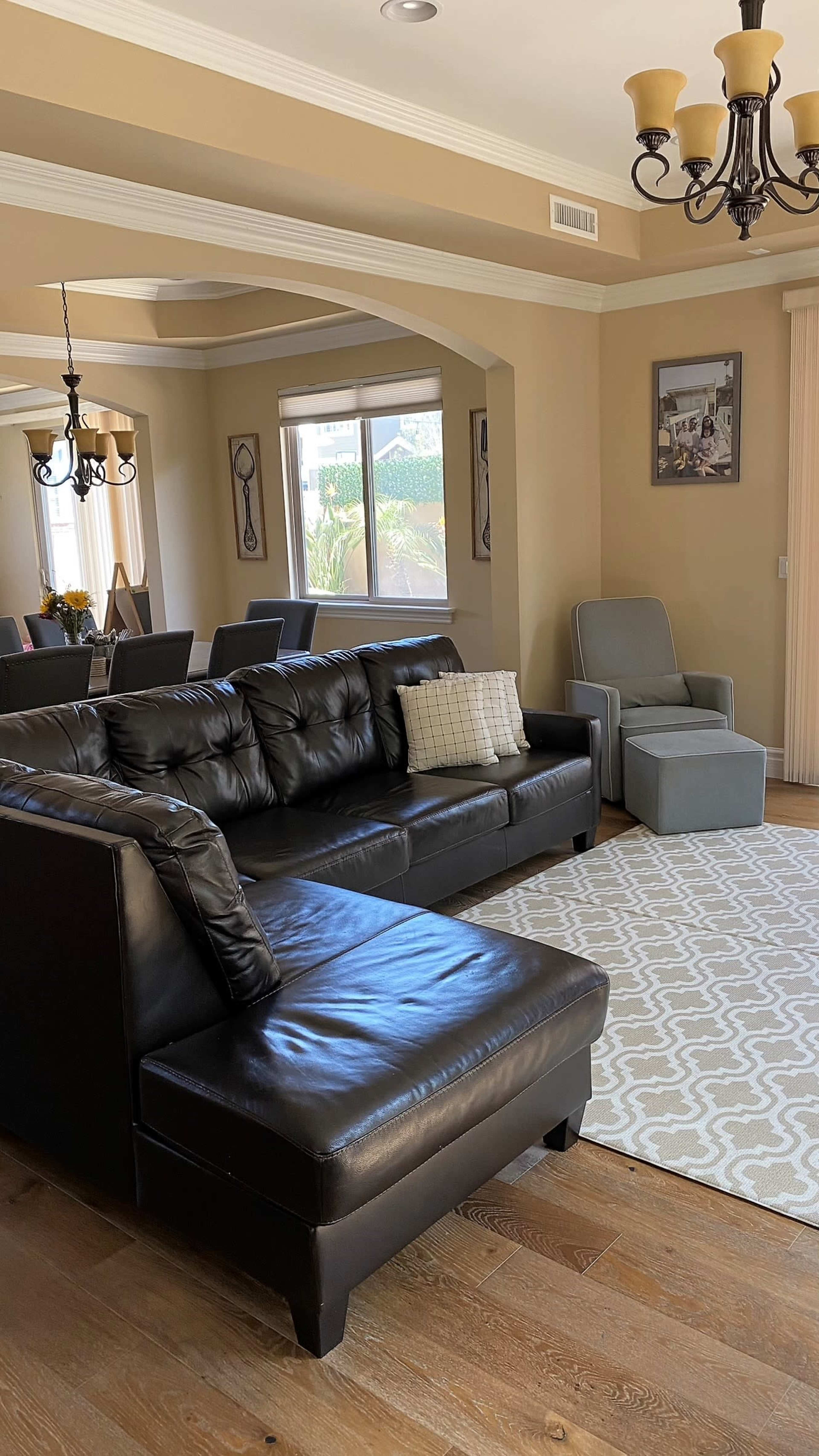 A living room with a black leather sectional sofa, a light gray armchair, and a patterned area rug on wooden flooring.