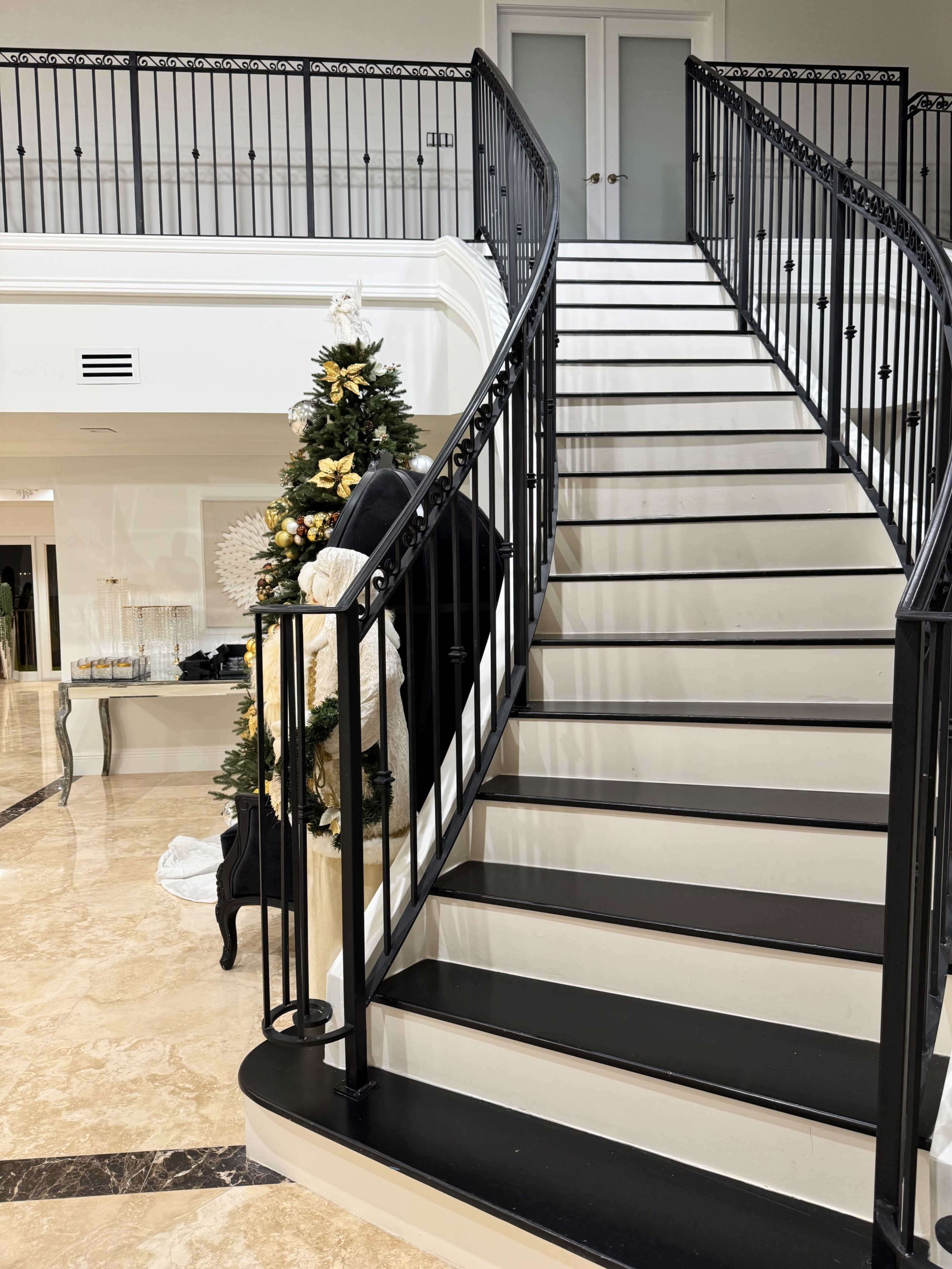 The image shows a curved staircase with black railing leading to an upper level, beside a decorated Christmas tree in a spacious entrance hall.
