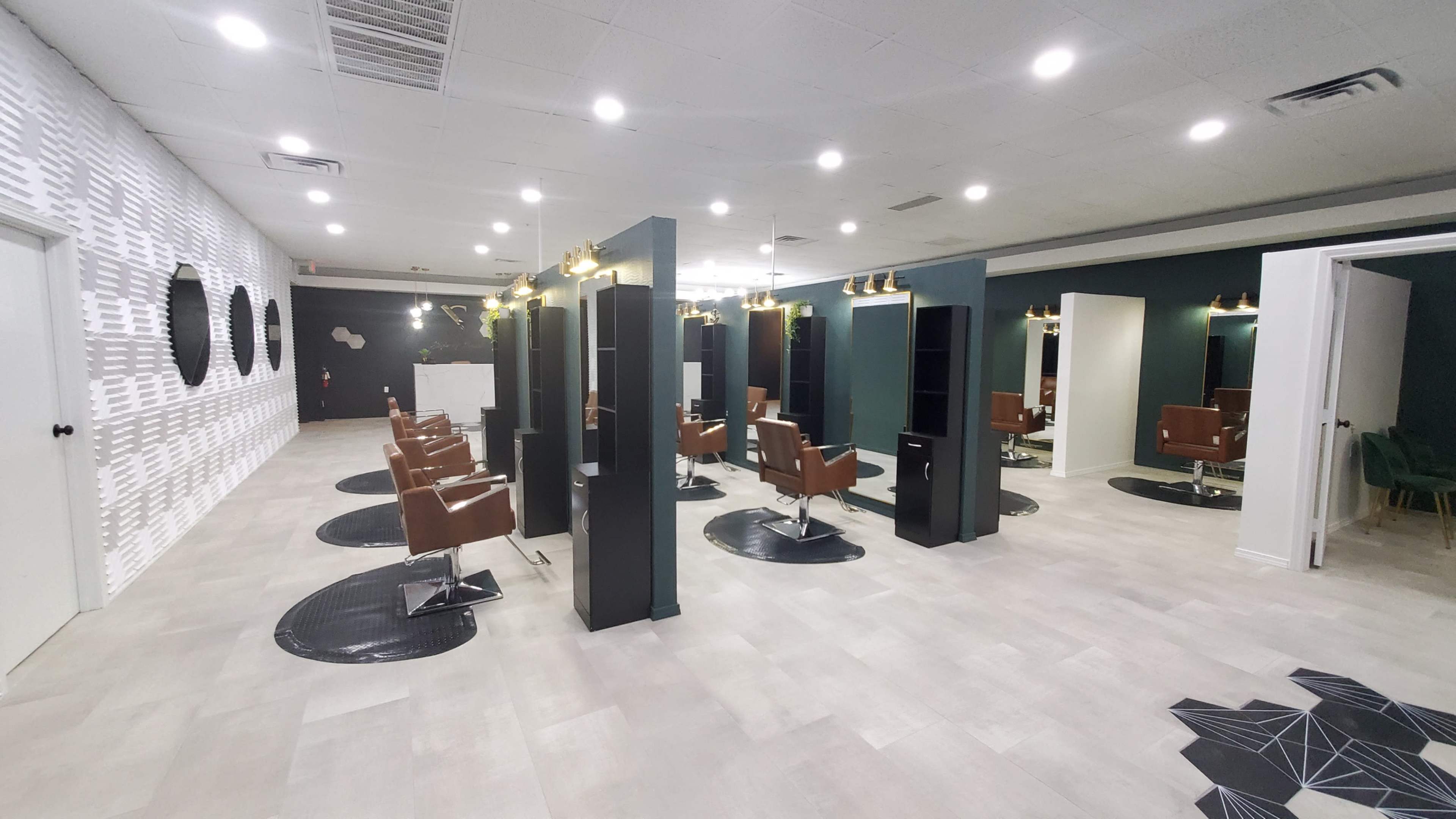The image shows a modern salon interior with multiple styling stations, each featuring brown chairs and illuminated mirrors, arranged on a light-colored floor.