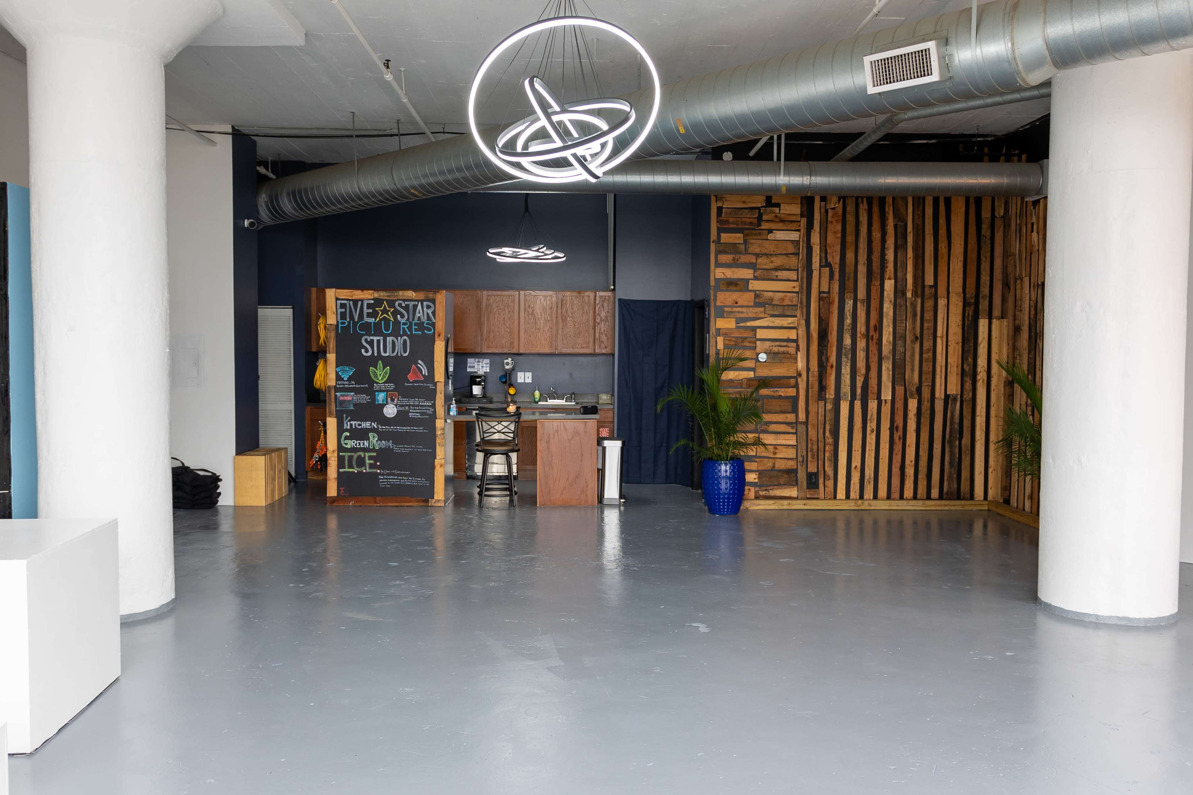 A spacious, modern studio with a kitchen area, a large wooden accent wall, and minimal furnishings, creating an open and uncluttered environment.