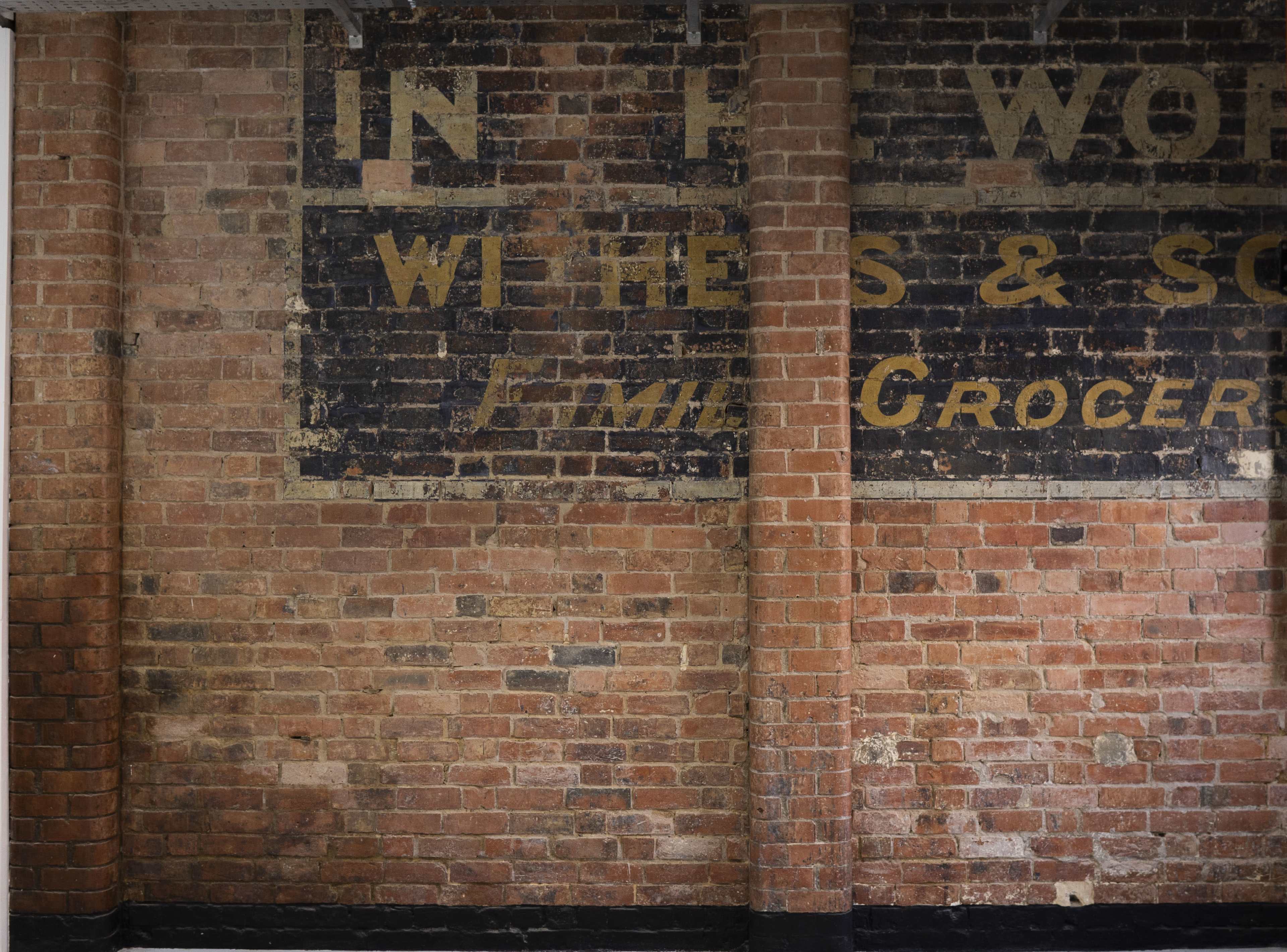 A brick wall with faded text advertising a grocery store.