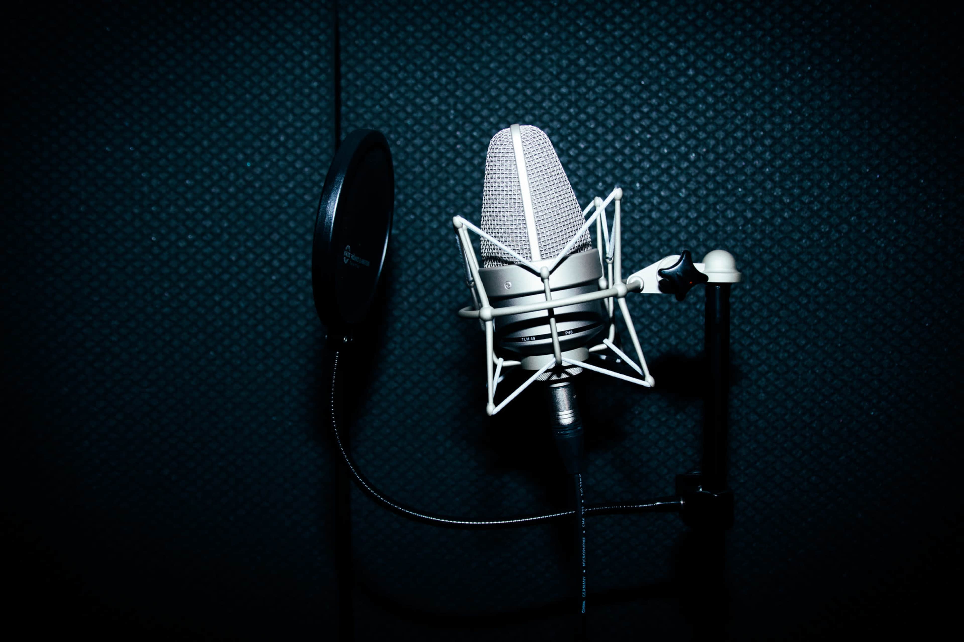 A microphone is positioned on a stand in a recording studio, with a pop filter attached nearby.
