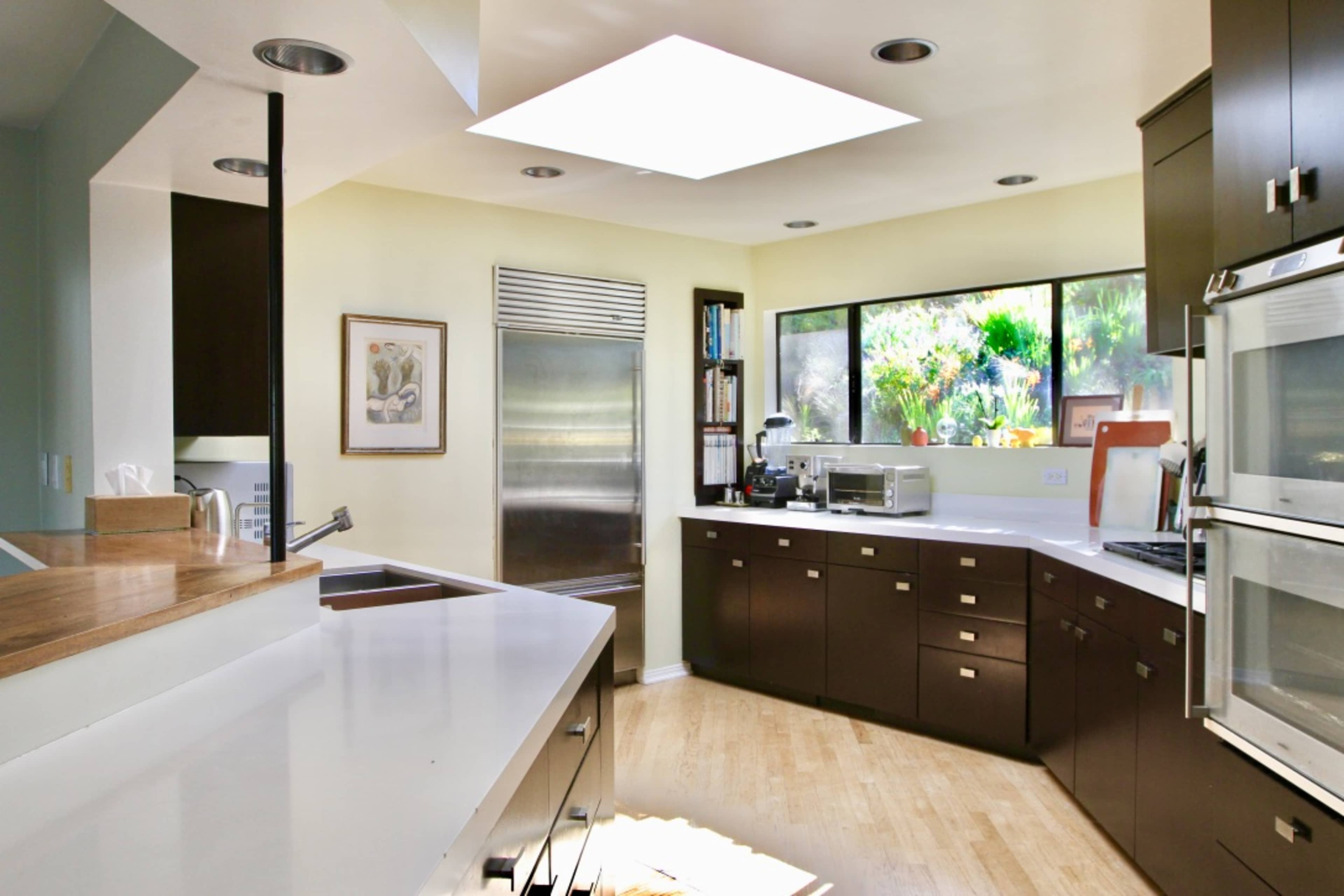 A modern kitchen with sleek cabinetry, a skylight overhead, and large windows offering a view of greenery outside.
