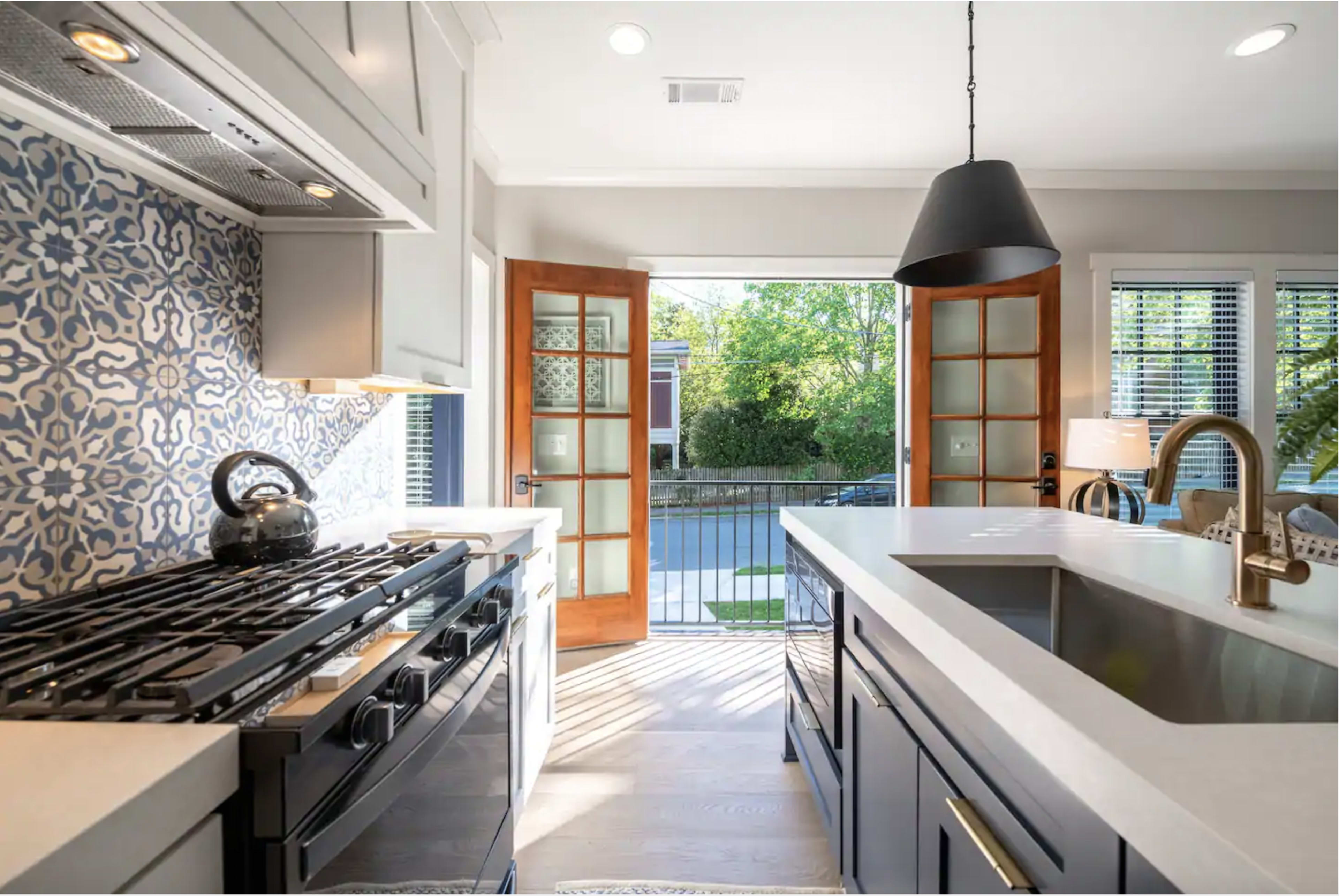 A modern kitchen features a gas stove, white countertops, and open doors leading to an outdoor space with natural light streaming in.