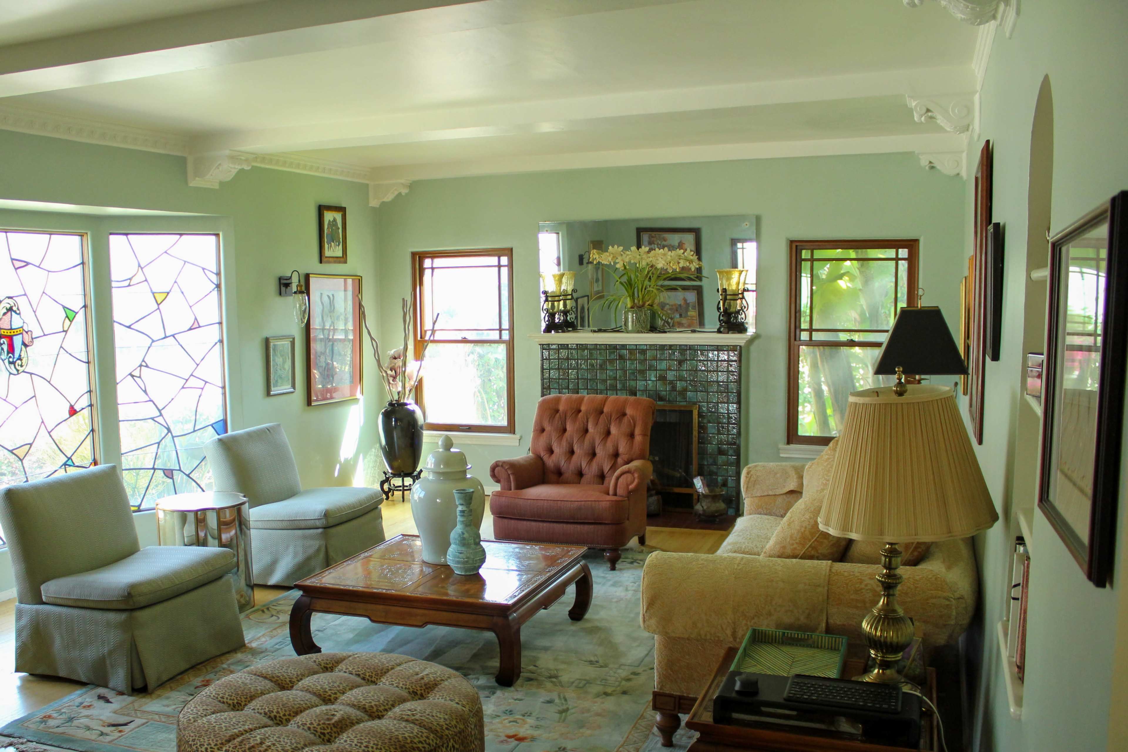 The living room features a blend of light-colored furniture, a tiled fireplace, and large windows with a stained glass design.