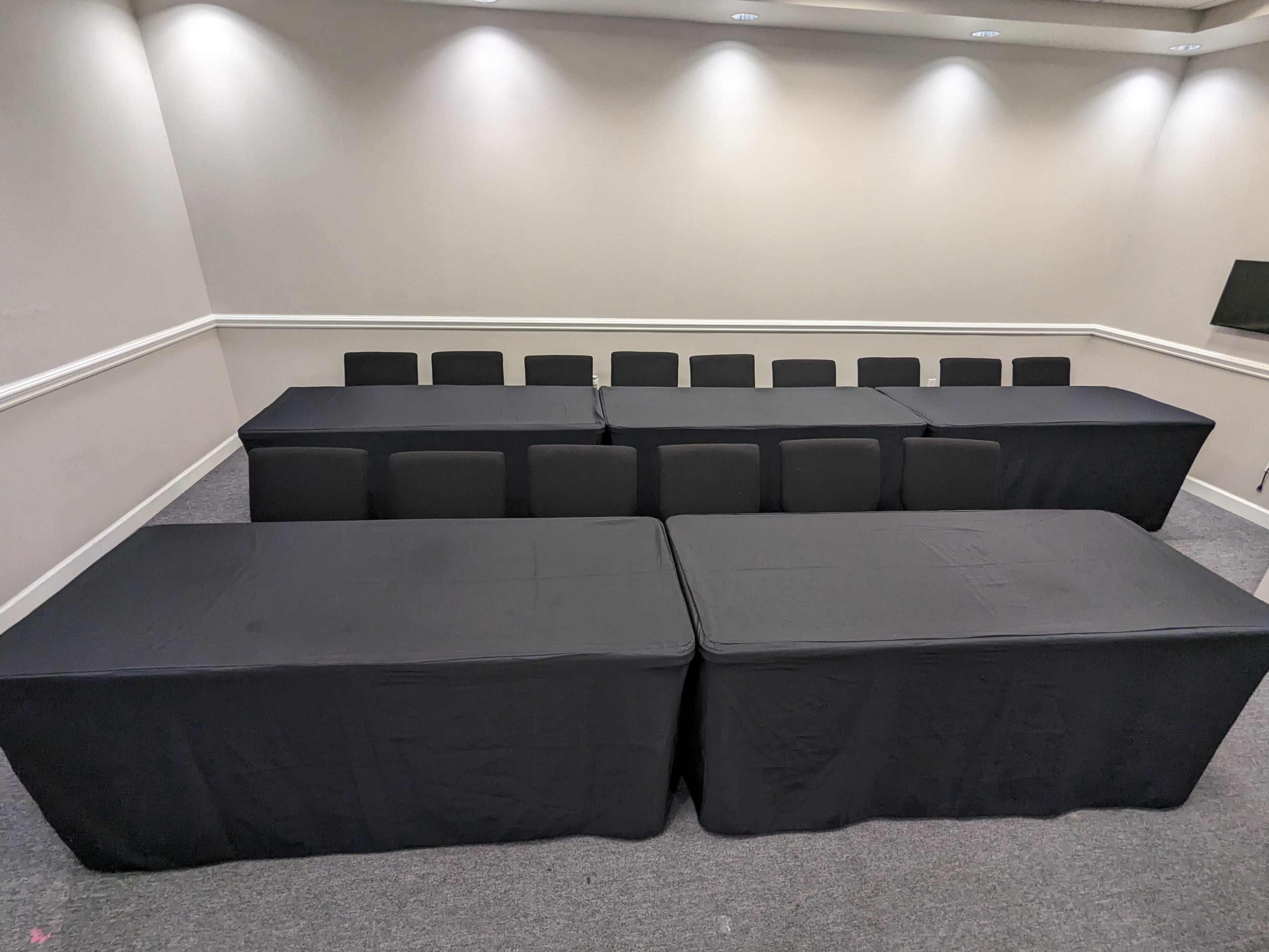 A conference room set up with multiple black-covered tables arranged in a rectangular formation, surrounded by black chairs.