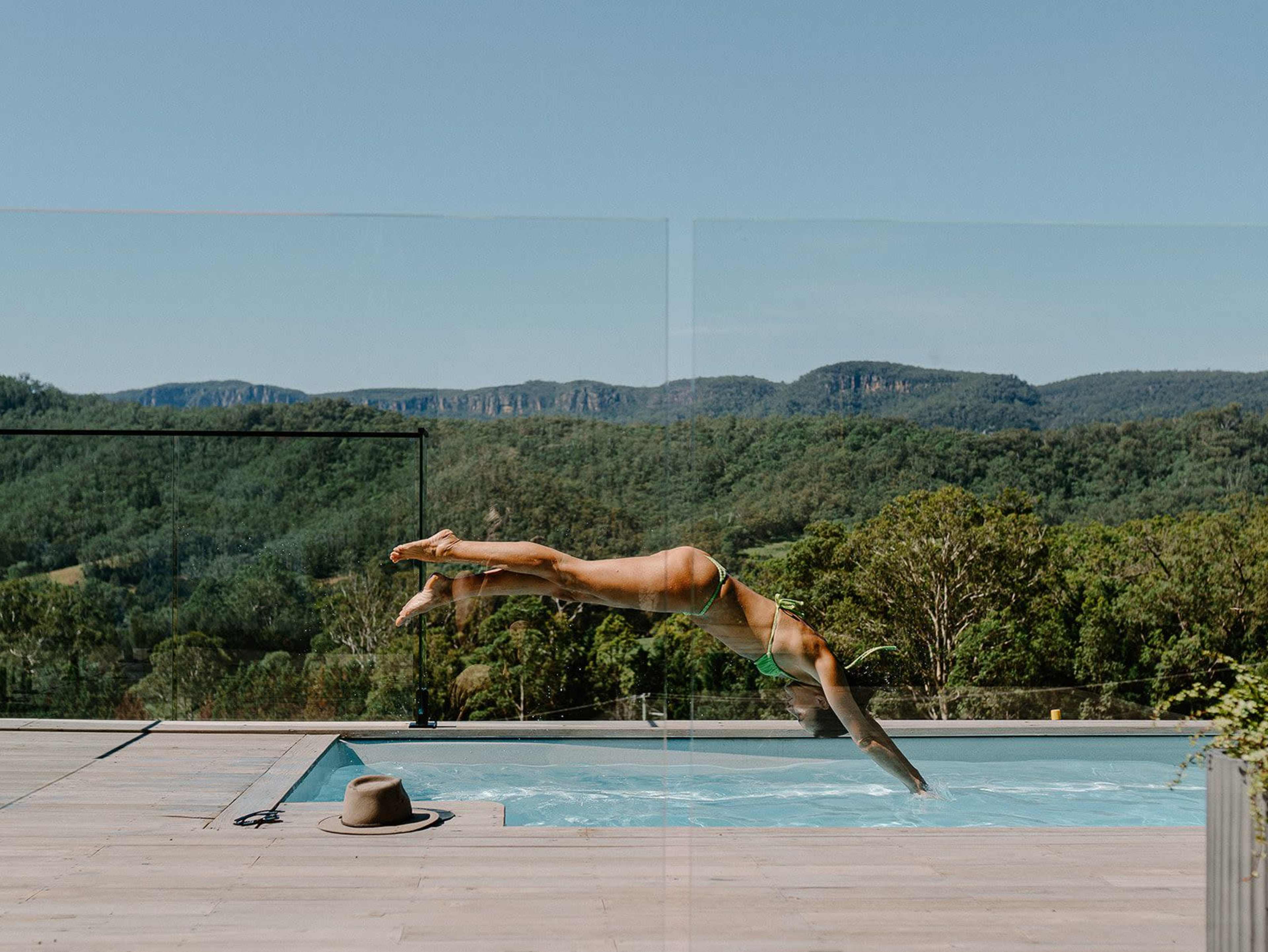 A person dives into a swimming pool surrounded by trees and mountains.