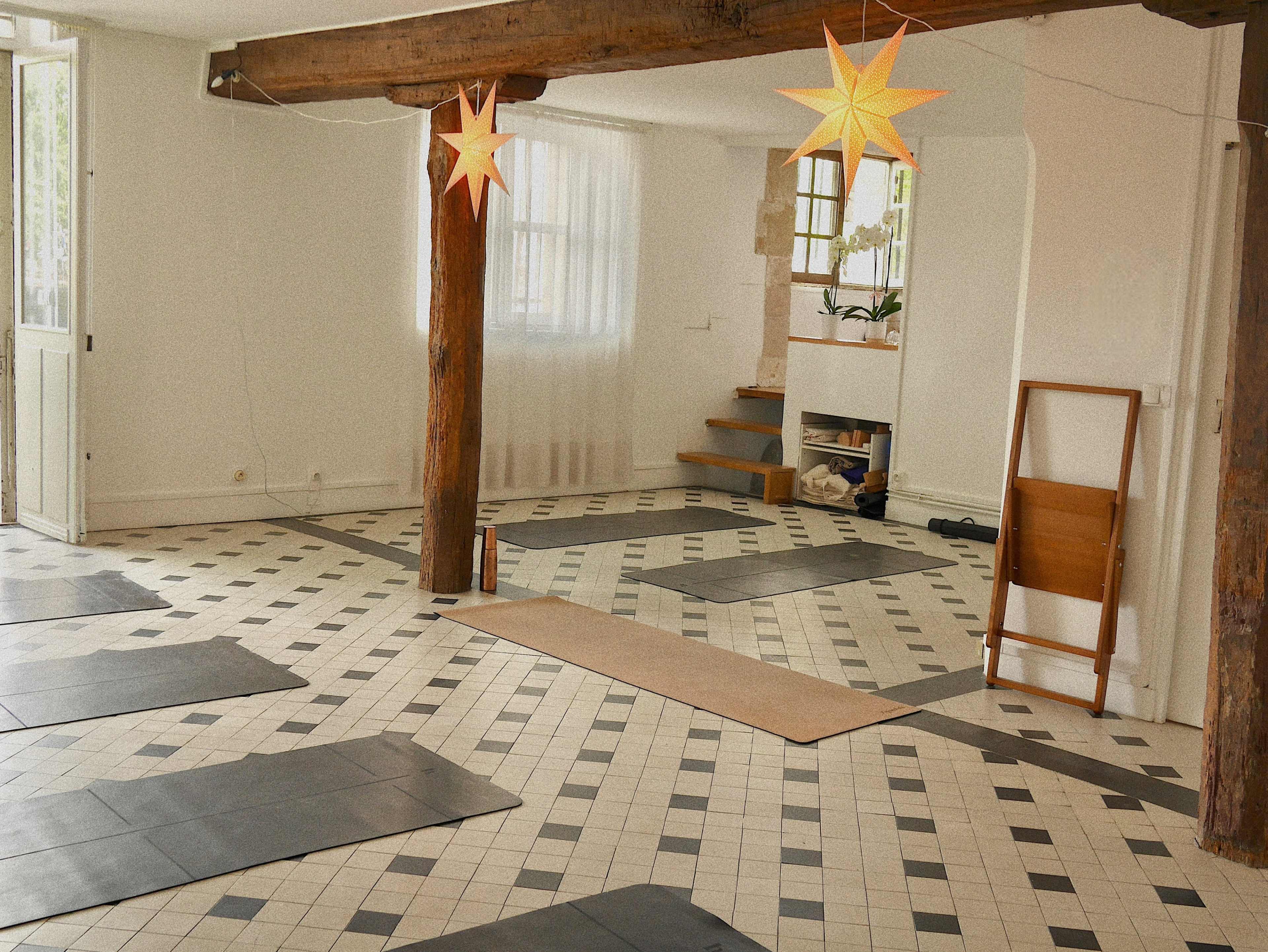 A yoga studio with black mats arranged on a tiled floor, featuring wooden beams and star-shaped paper lanterns hanging from the ceiling.