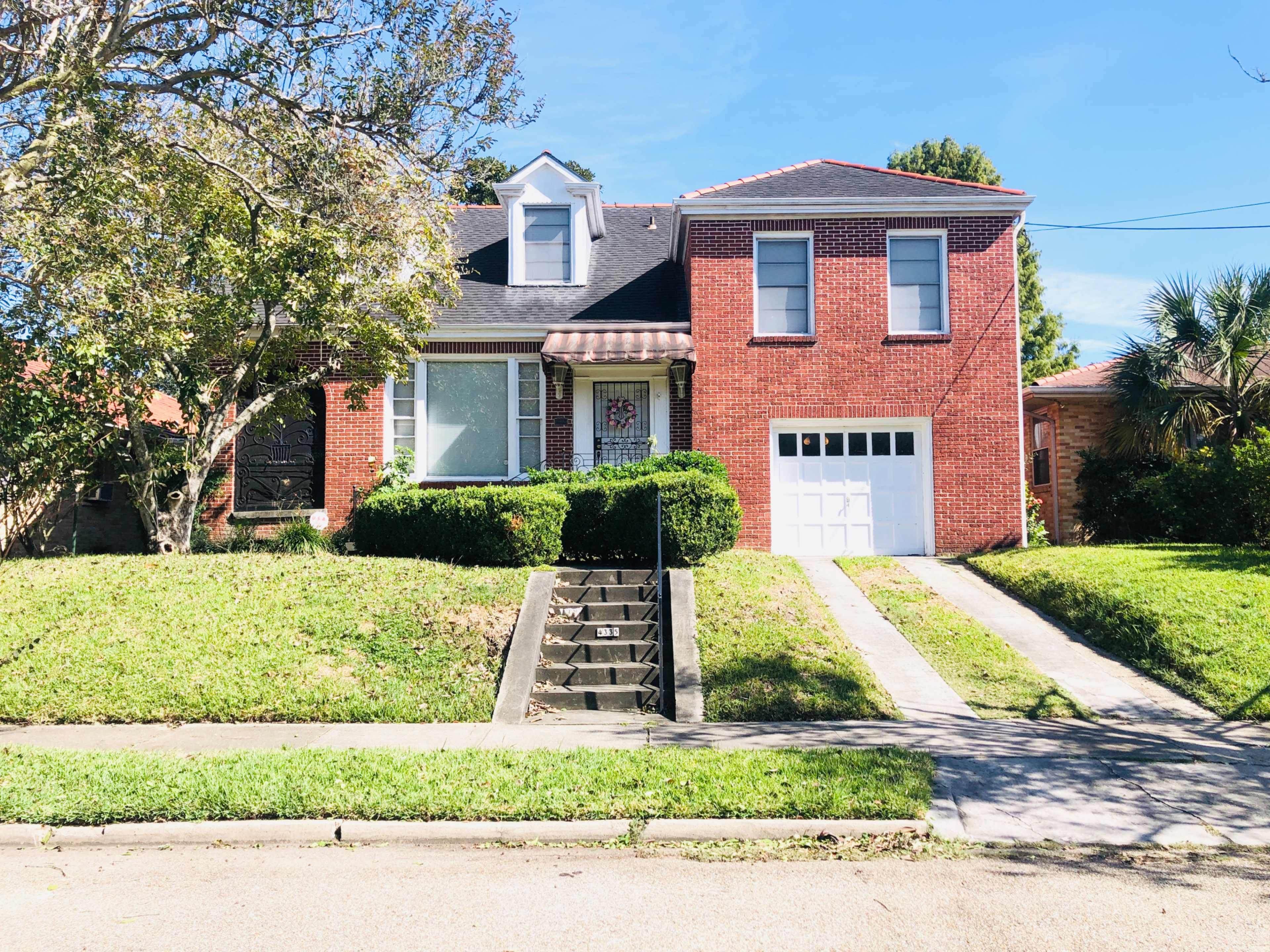 A two-story red brick house with a front garden and a driveway leading to a garage.