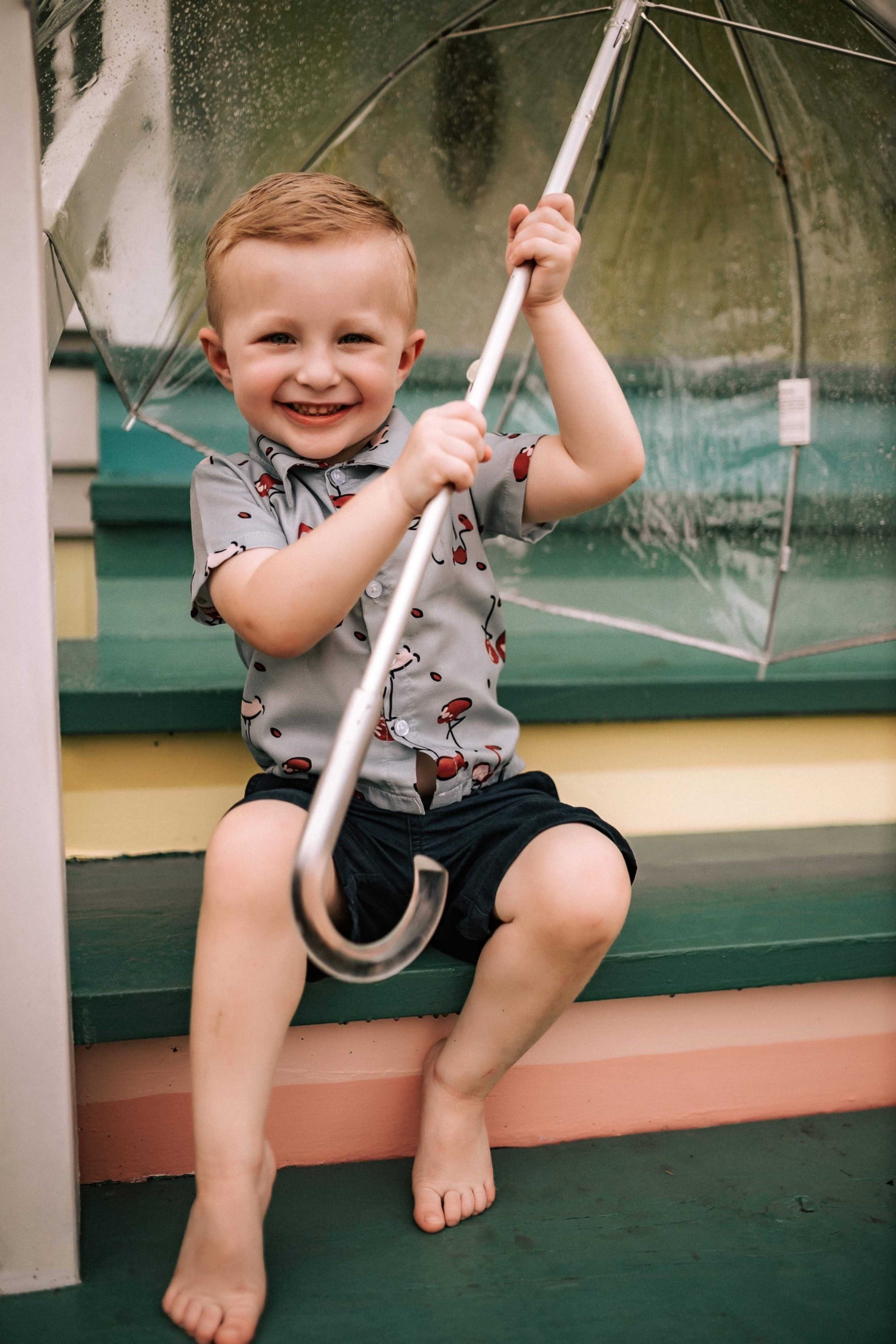 A smiling child sits on colorful steps holding a transparent umbrella.